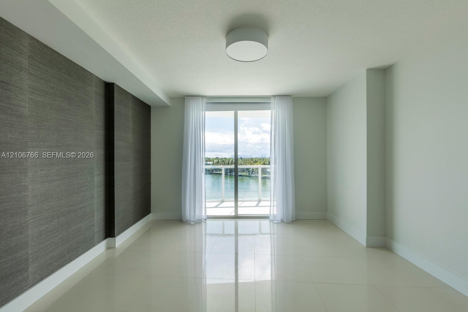Interior space featuring large-format tile flooring, textured charcoal accent wall, flush-mount ceiling lighting, and sliding glass doors leading to a balcony