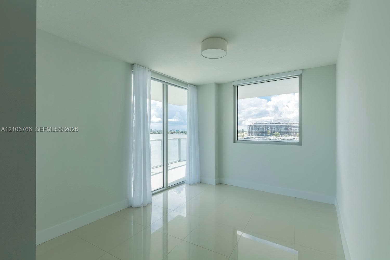 Interior space featuring large-format tile flooring, ceiling-mounted drum lighting, floor-to-ceiling glass sliding door, and a multi-pane window with water and structural scenery