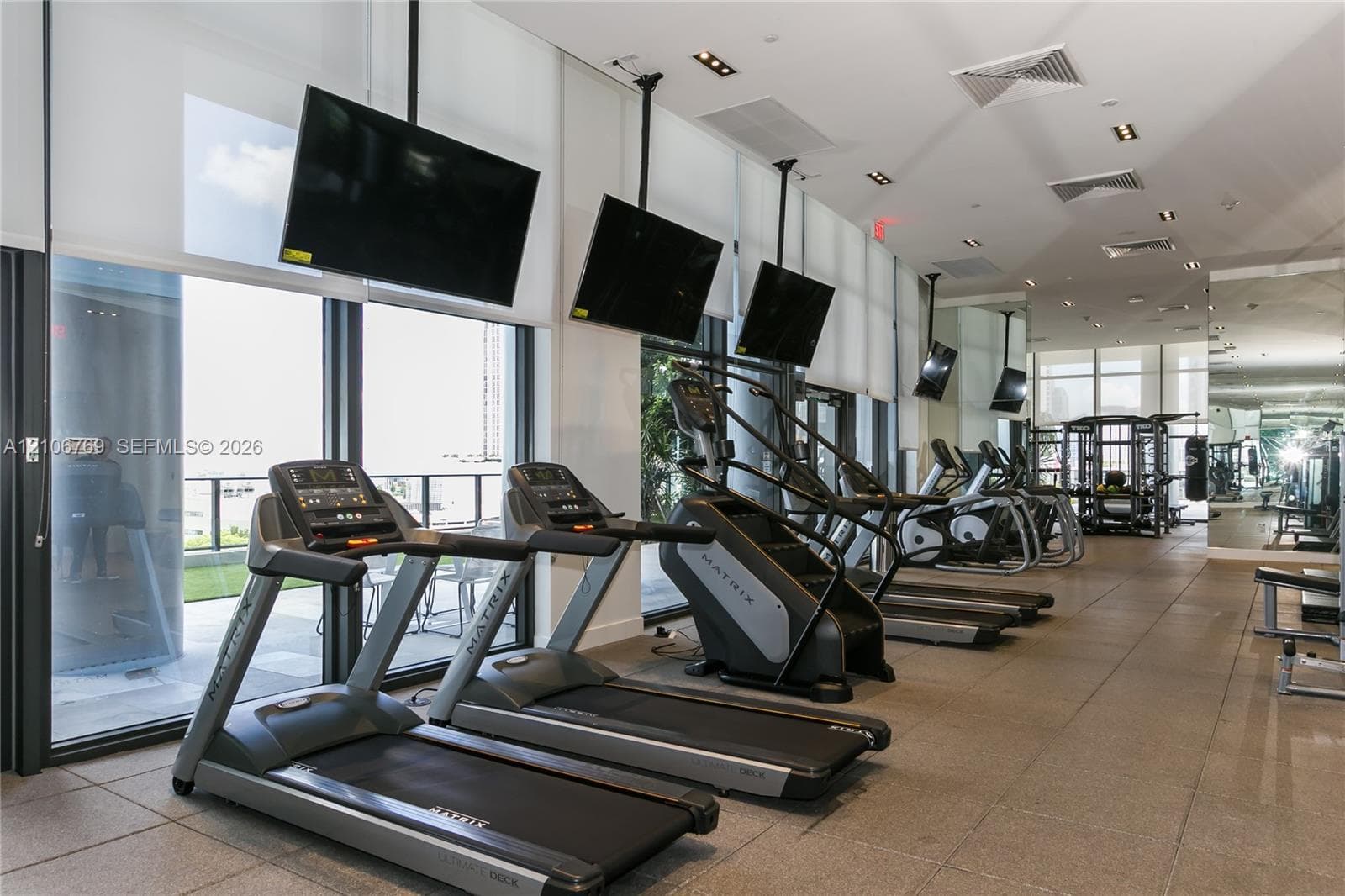 Fitness center featuring floor-to-ceiling windows, recessed lighting, tile flooring, and wall-mounted televisions