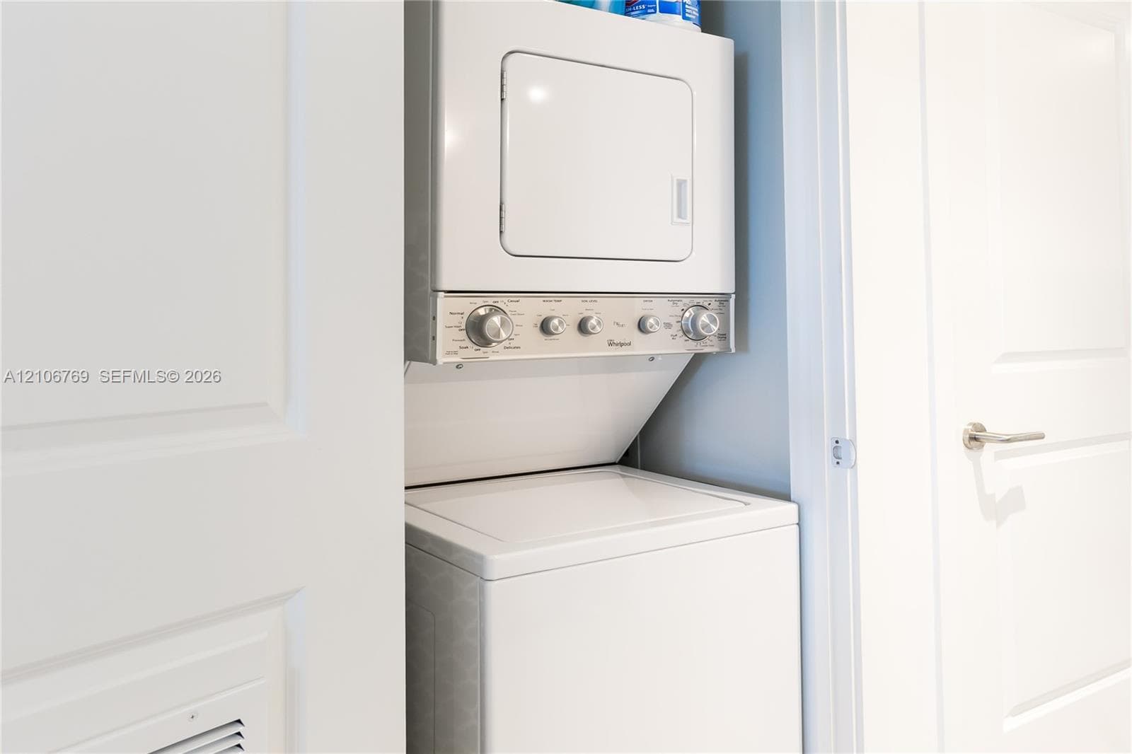 Stacked white washer and dryer unit housed within a recessed closet featuring white paneled interior doors and brushed metal hardware