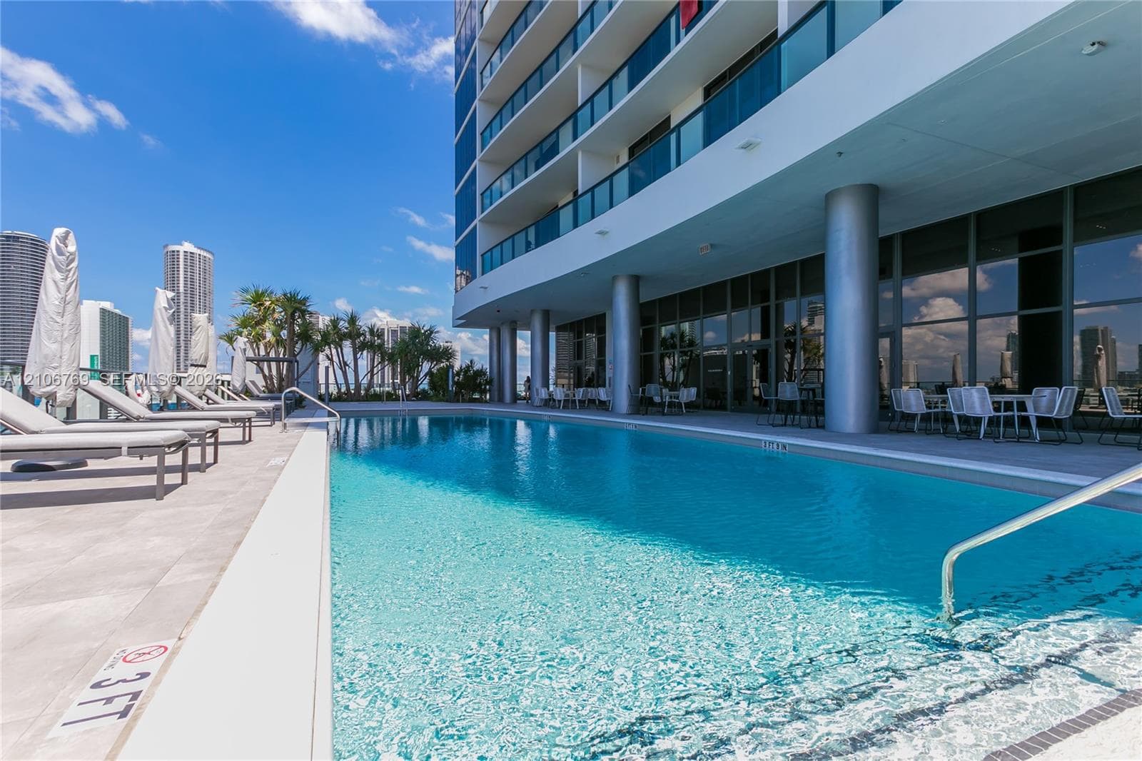 Outdoor swimming pool featuring a concrete deck, glass balcony railings, structural pillars, and floor-to-ceiling windows