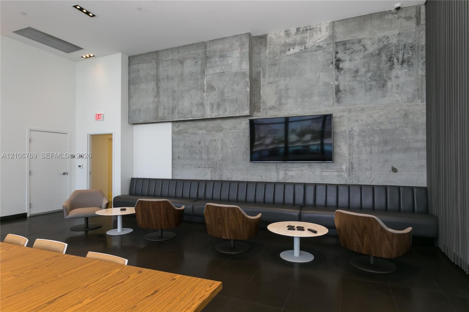 Exposed concrete accent wall featuring large-format paneling, high ceilings, recessed lighting, and dark tile flooring