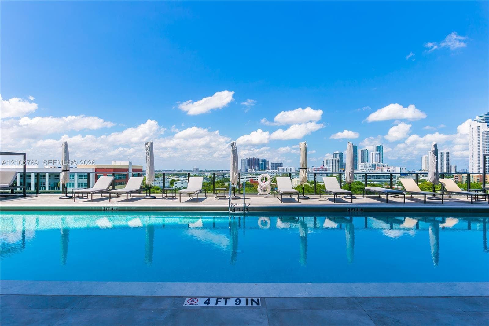 Rooftop swimming pool featuring stone-style decking, a metal perimeter railing, and an urban skyline backdrop