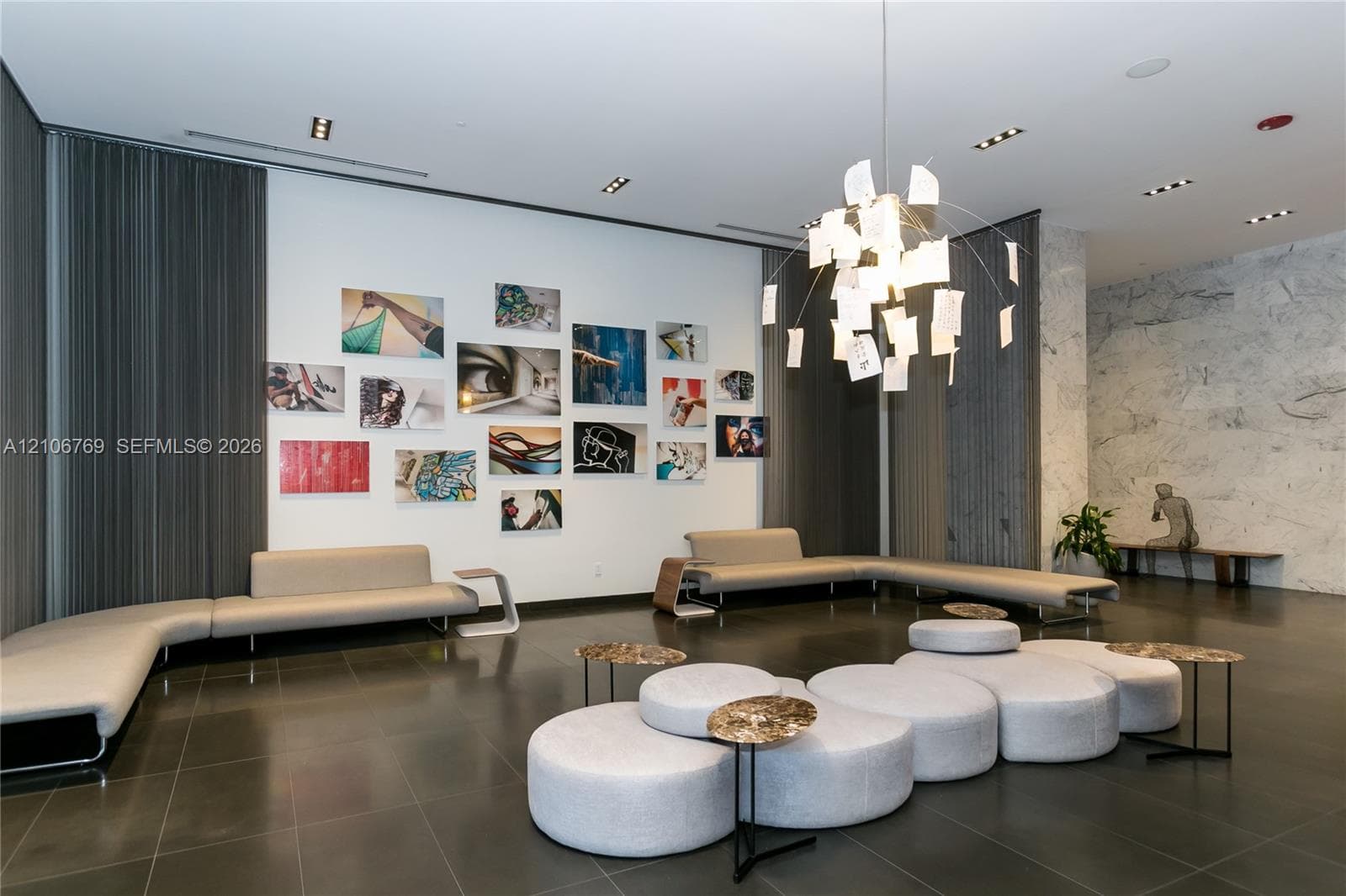 Modern lobby featuring large-format tile flooring, stone-clad accent wall, recessed lighting, and a suspended statement chandelier