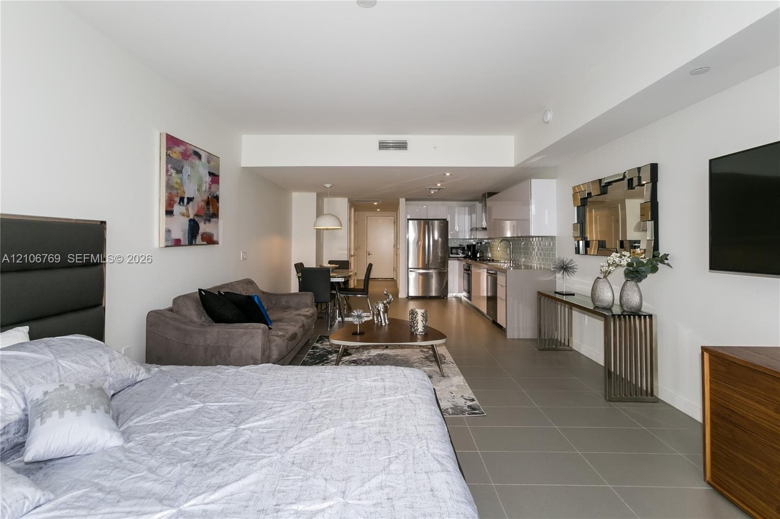 Open-concept studio featuring large-format tile flooring, recessed lighting, and a modern kitchen with stainless steel appliances and glossy cabinetry