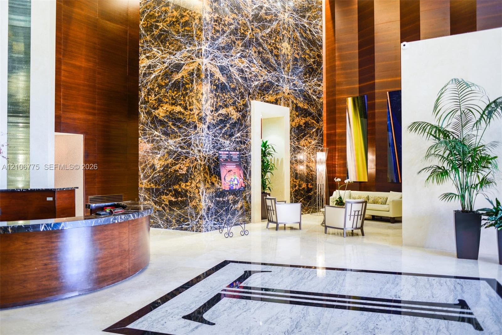 Grand lobby featuring soaring ceilings, full-height decorative stone cladding, curved wood-paneled reception desk, and polished stone flooring with geometric inlay