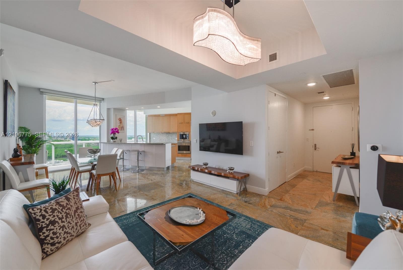 Living area featuring stone flooring, a tray ceiling with a contemporary chandelier, and floor-to-ceiling windows