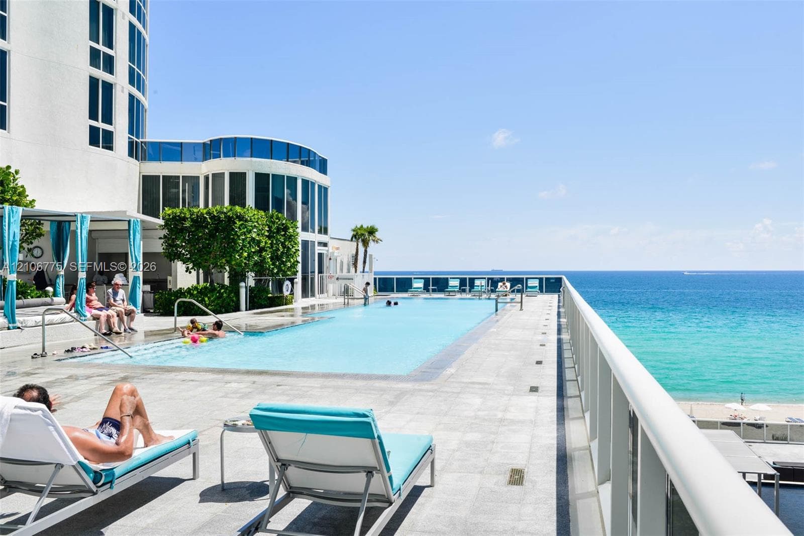 Oceanfront deck featuring a rectangular swimming pool, stone-tile flooring, and glass-paneled perimeter railing