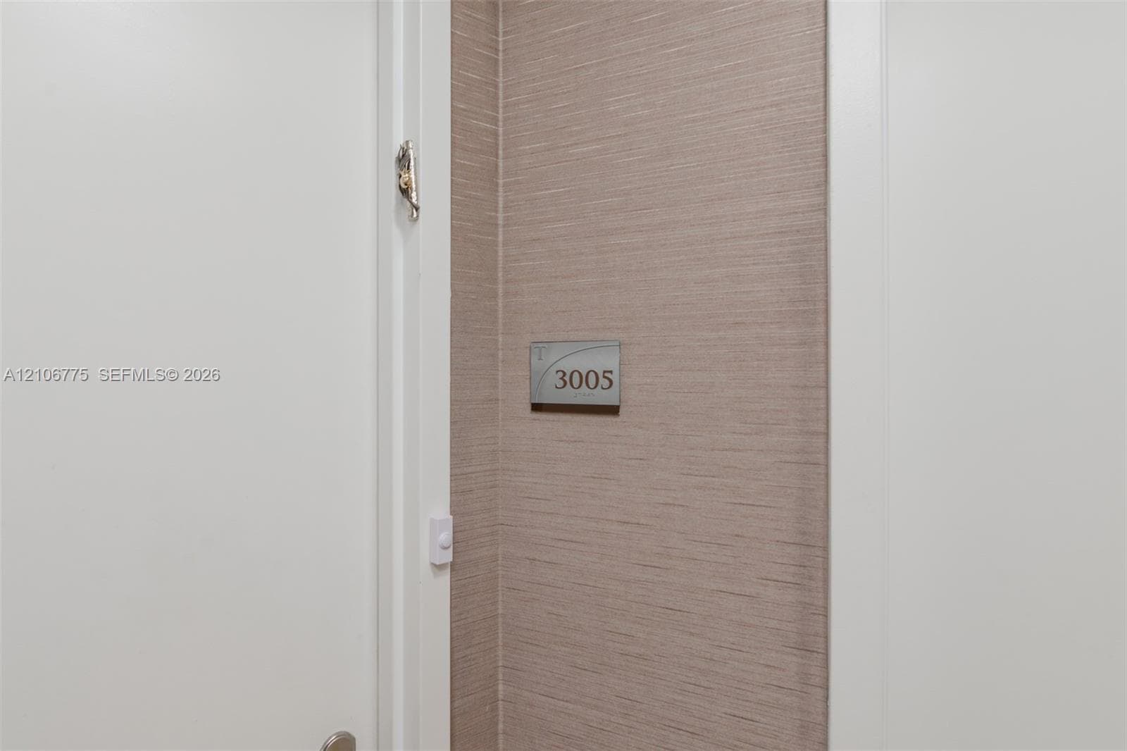 Textured wall covering in a neutral finish with a brushed metal unit identification plaque and white door trim