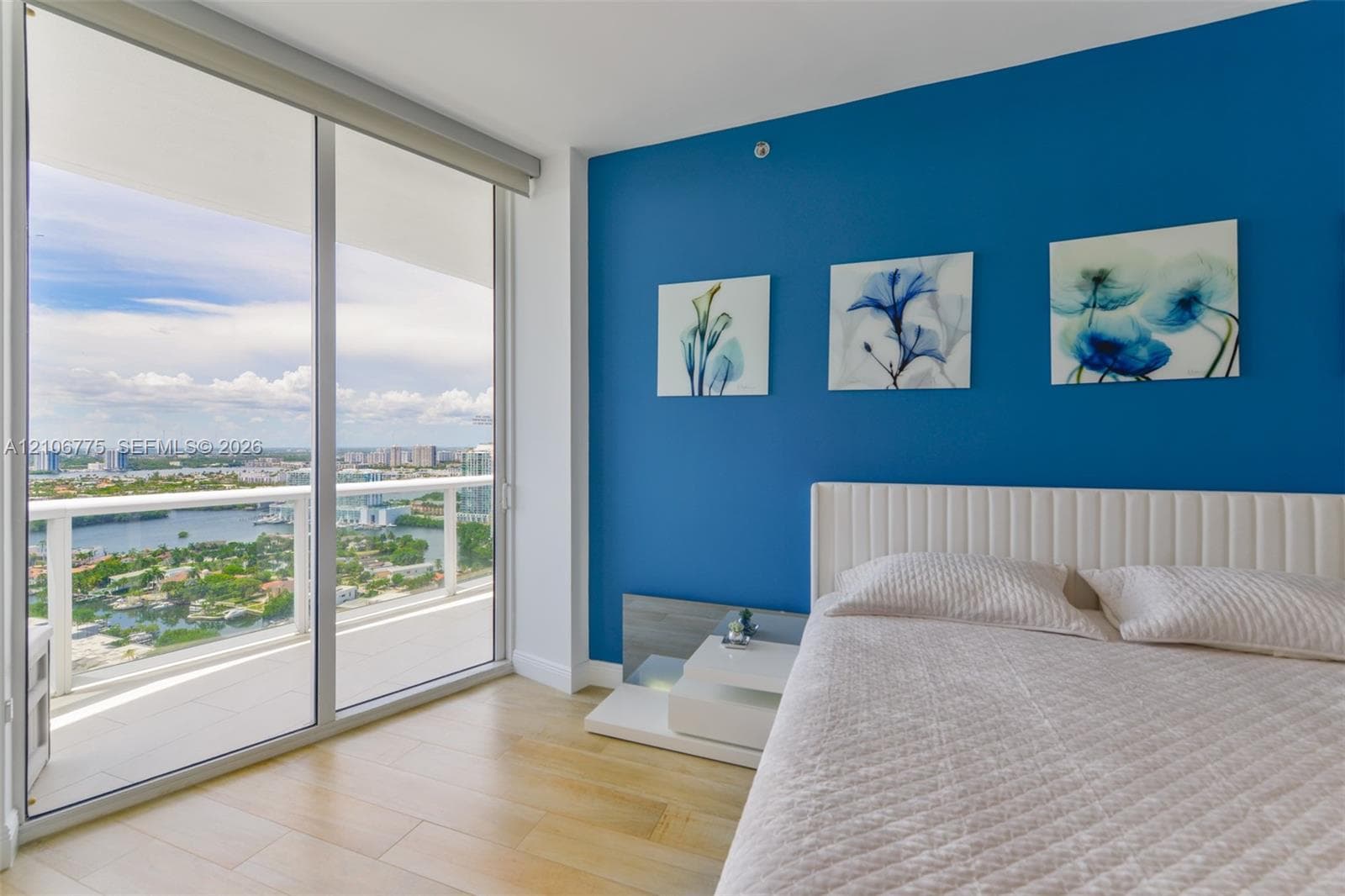 Floor-to-ceiling glass sliding doors opening to a private balcony, wood-finish flooring, and an expansive cityscape backdrop