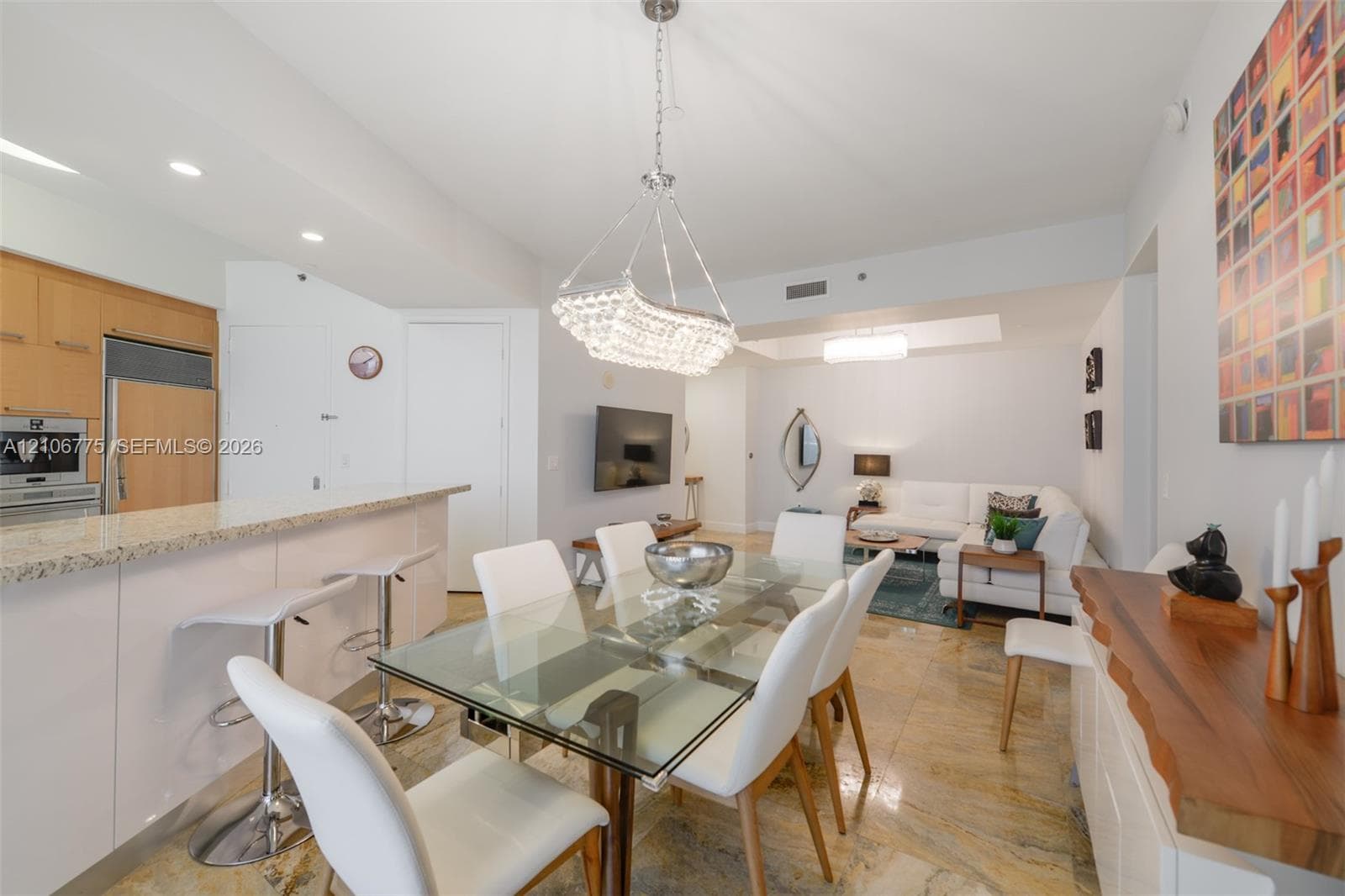 Kitchen featuring stone countertops, integrated stainless steel appliances, and wood-finish cabinetry, complemented by polished stone flooring and a crystal-accented chandelier