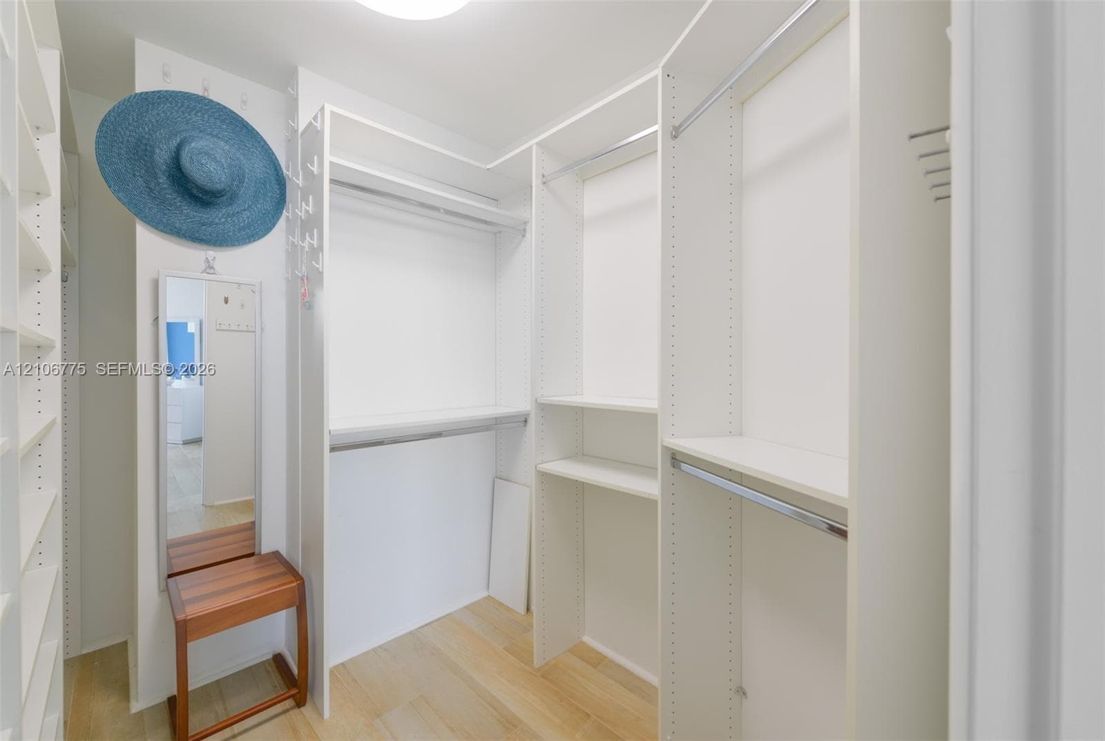 Walk-in closet featuring white laminate built-in cabinetry, adjustable shelving, metal hanging rods, and wood-finish flooring