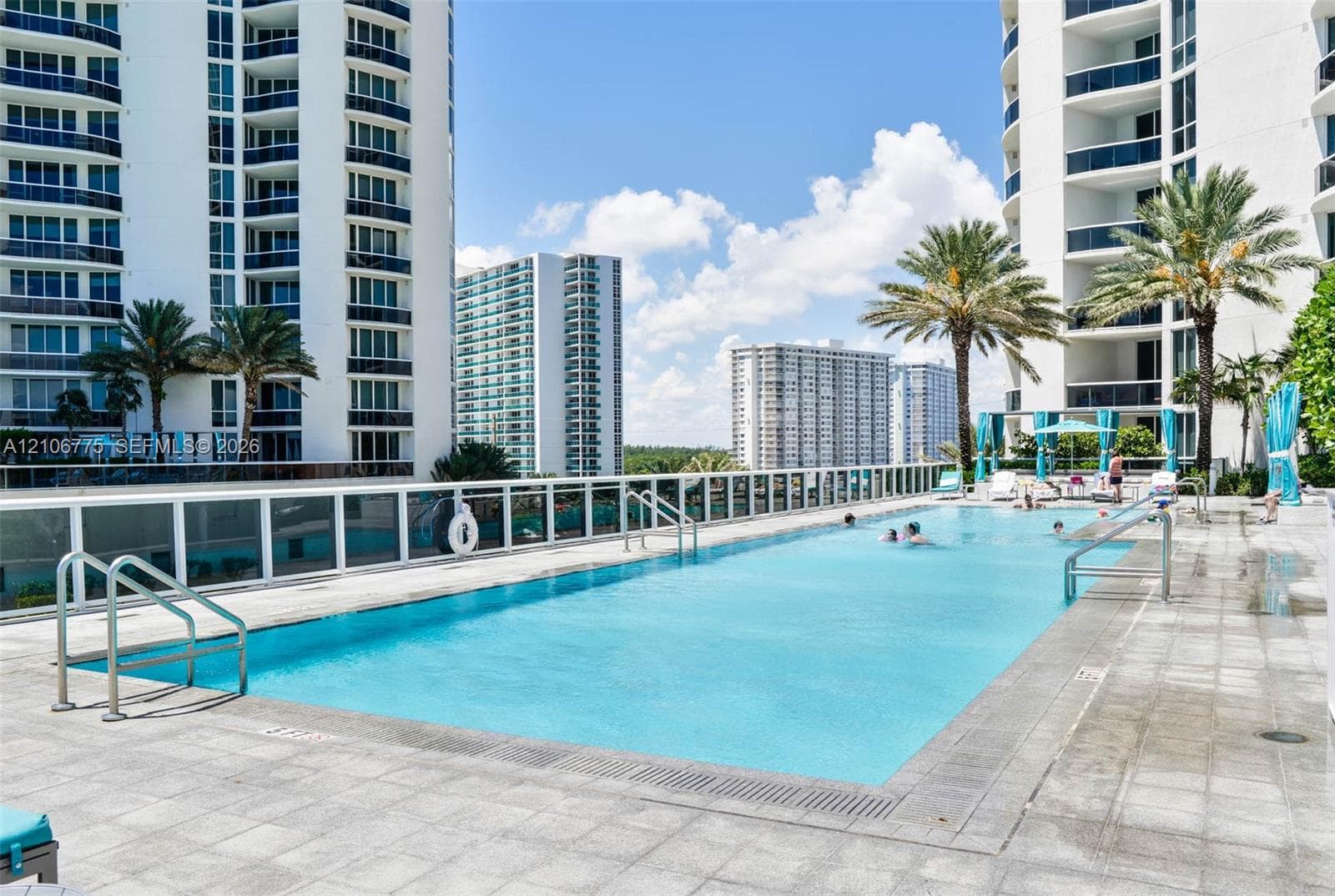 Swimming pool featuring a tiled deck, perimeter safety railing, metal entry ladders, and palm landscaping