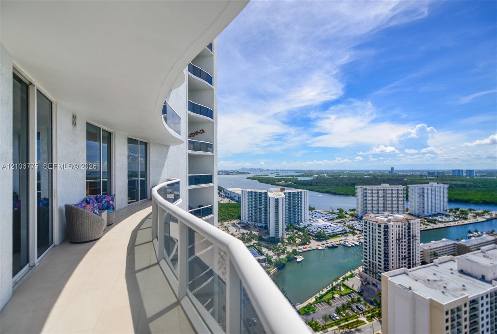 Curved balcony featuring light-toned tile flooring, floor-to-ceiling glass sliding doors, and a transparent railing with a metal top rail