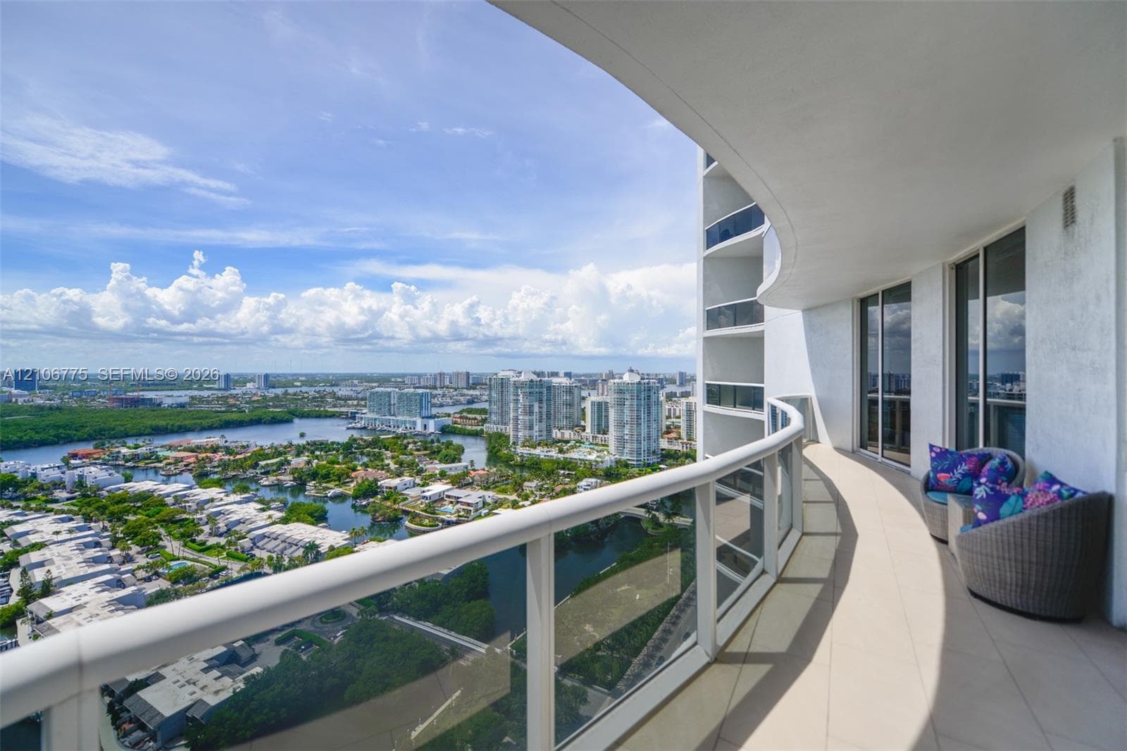 Curved private balcony featuring large-format tile flooring and a glass-panel railing with a top rail