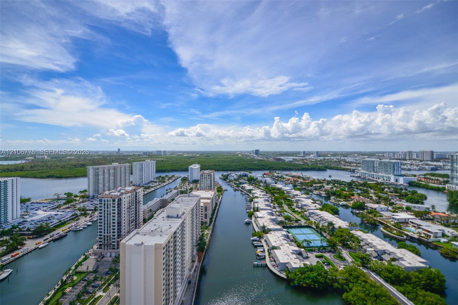 Aerial perspective showcasing high-rise residential architecture, expansive waterway access, manicured tennis courts, and mature coastal vegetation