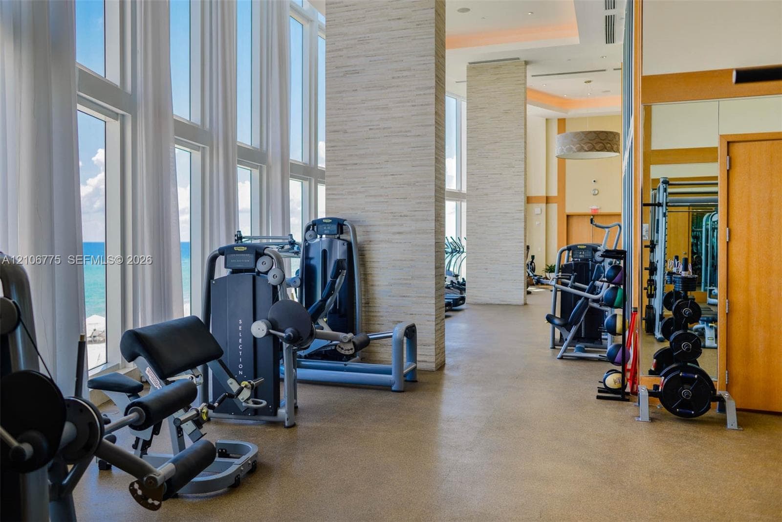 Fitness center featuring floor-to-ceiling windows, stone-clad structural columns, high ceilings, and mirrored walls