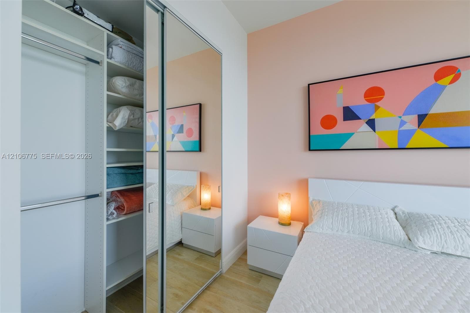 Built-in closet featuring adjustable shelving, hanging rods, and sliding mirrored doors, complemented by wood-finish flooring