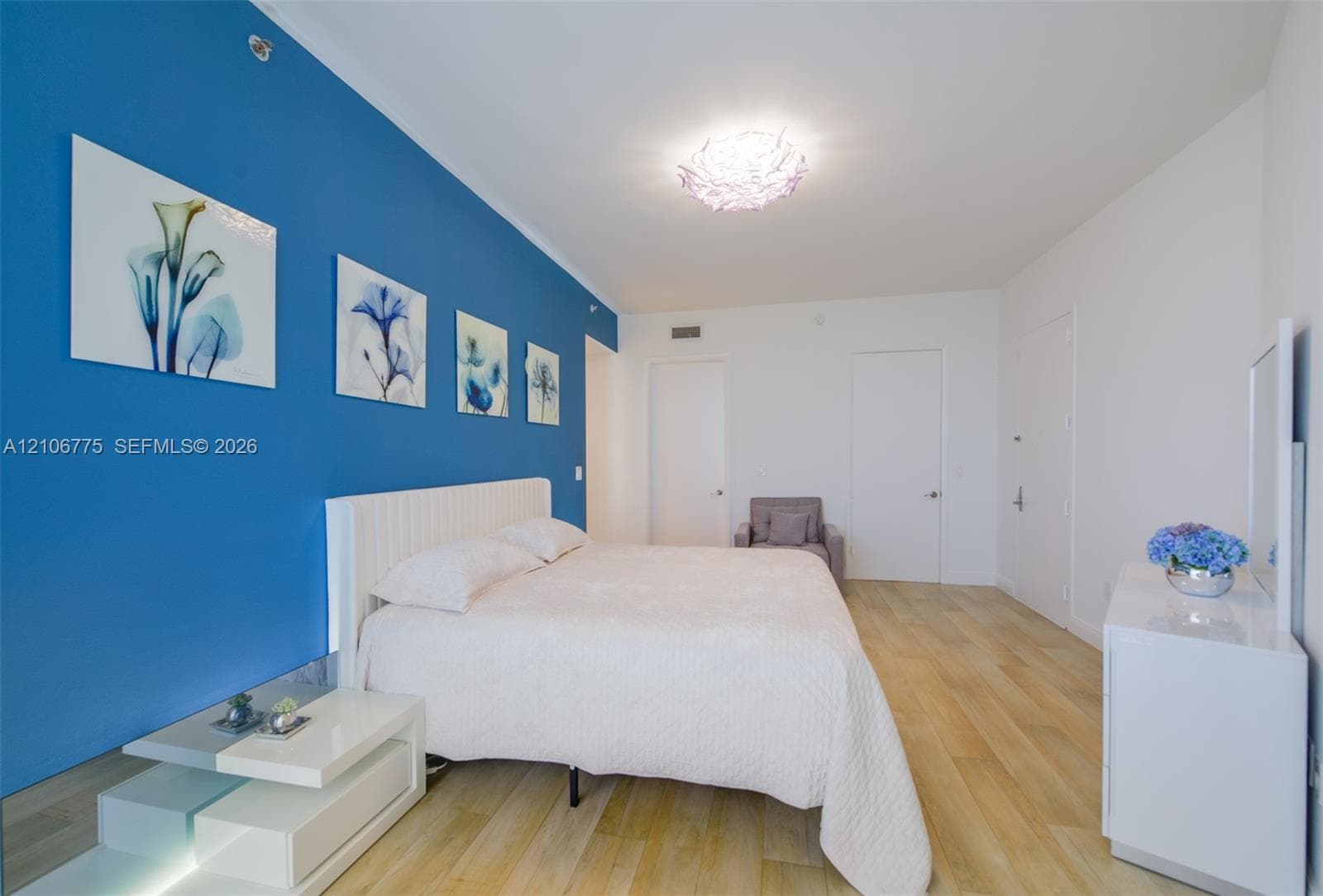 Spacious room featuring wood-finish flooring, a bold blue accent wall, and a unique textured circular flush-mount ceiling light fixture