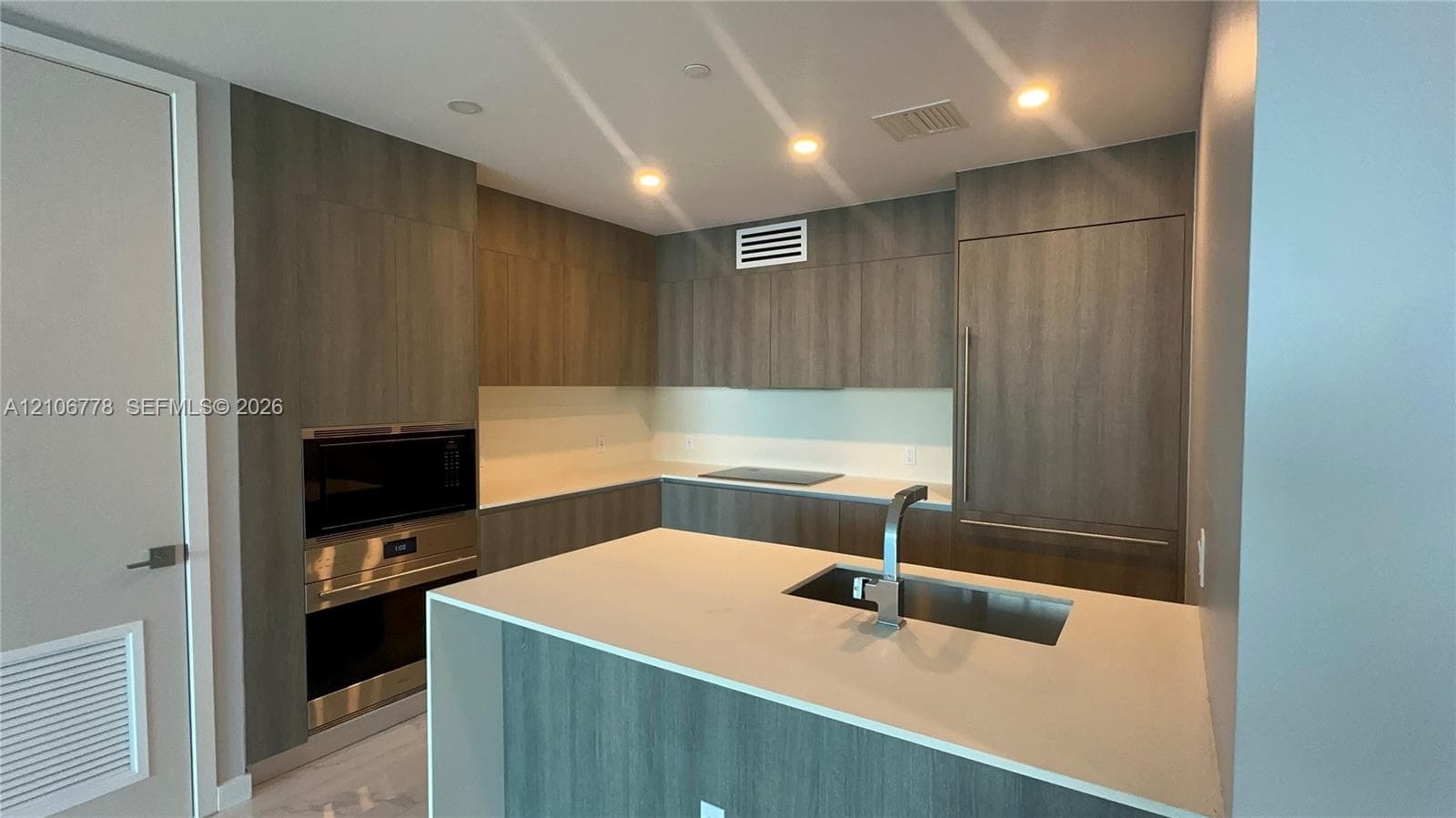 Modern kitchen featuring wood-finish cabinetry, integrated built-in appliances, a center island with an undermount sink, and recessed lighting