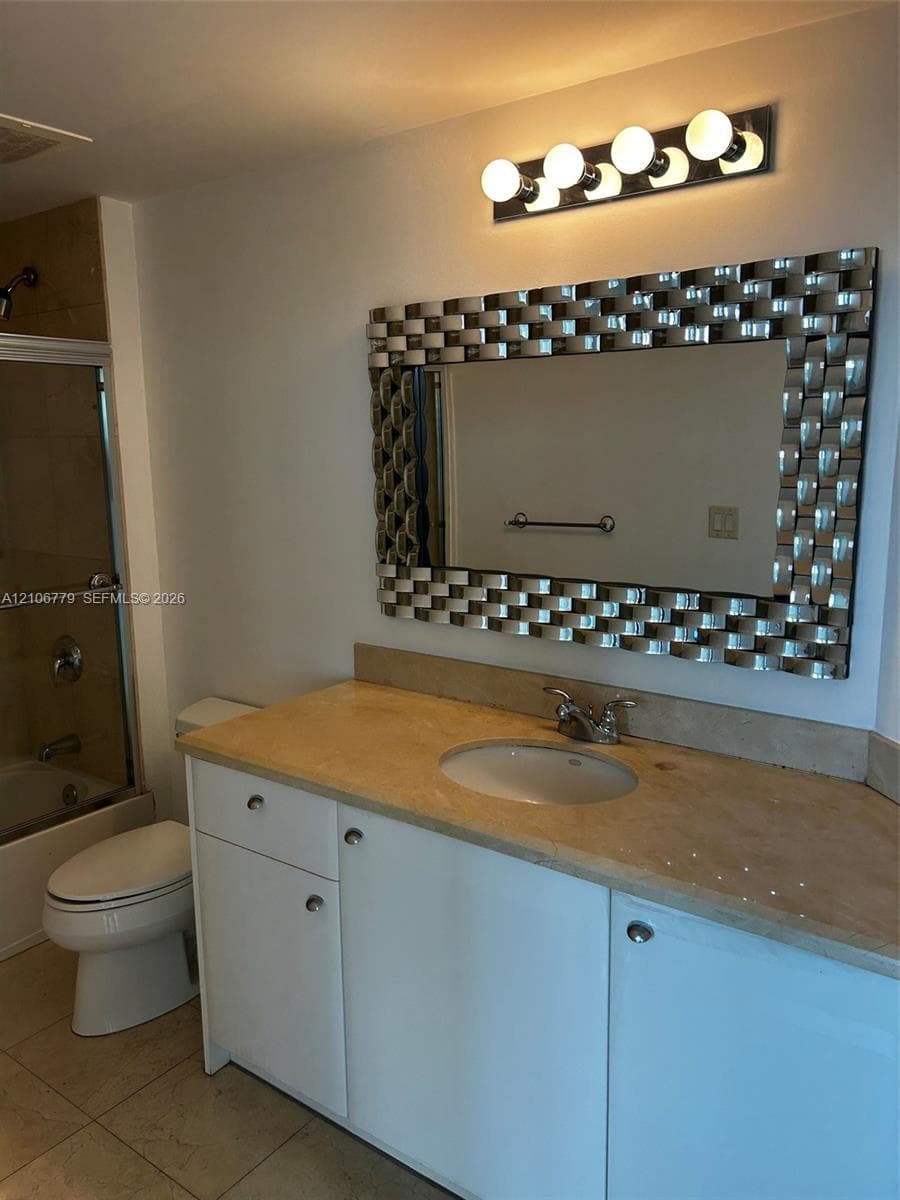 Bathroom vanity featuring white cabinetry, a neutral-toned stone-finish countertop, an oval undermount sink, a metallic basket-weave framed mirror, and a multi-globe light fixture