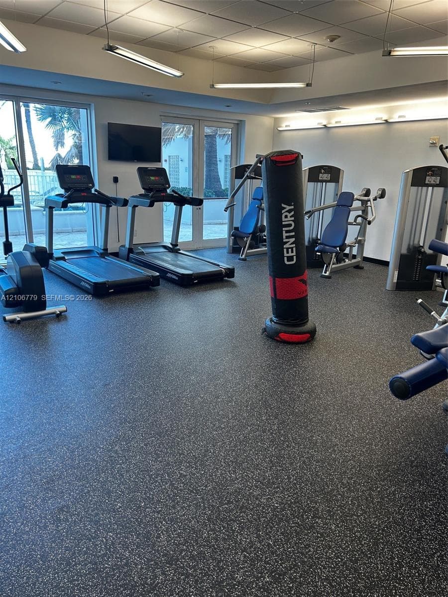Fitness center featuring durable speckled rubber flooring, suspended linear lighting, and large windows with direct exterior access