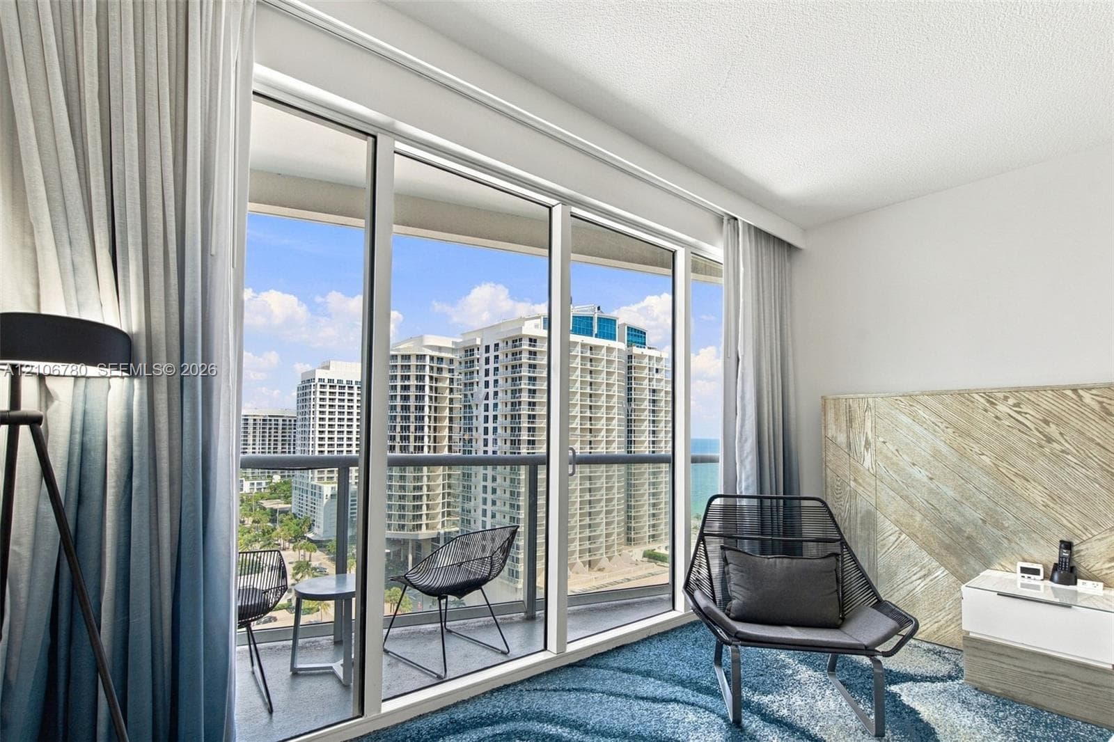 Floor-to-ceiling windows, private balcony with metal railing, and decorative wood-panel accent wall