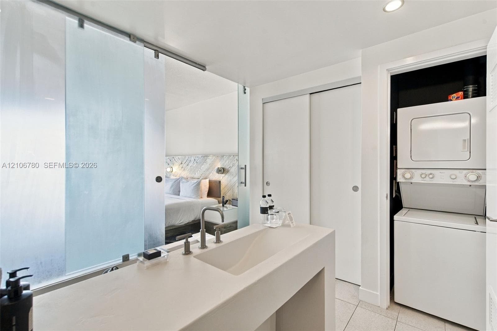 Solid-surface vanity featuring an integrated sink, polished metal widespread faucet, translucent glass sliding privacy partition, and built-in stacked laundry unit