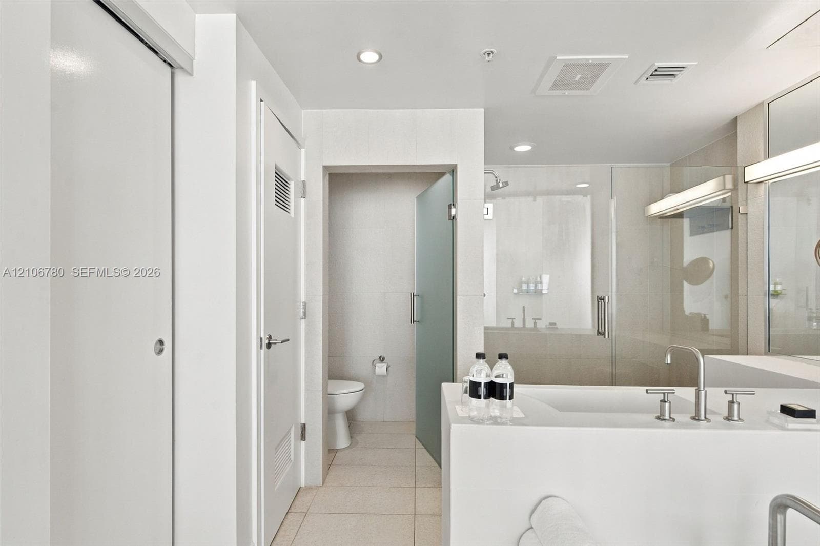 Bathroom featuring a vanity with a deck-mounted faucet, a glass-enclosed shower, a separate water closet with a frosted glass door, tile flooring, and recessed lighting