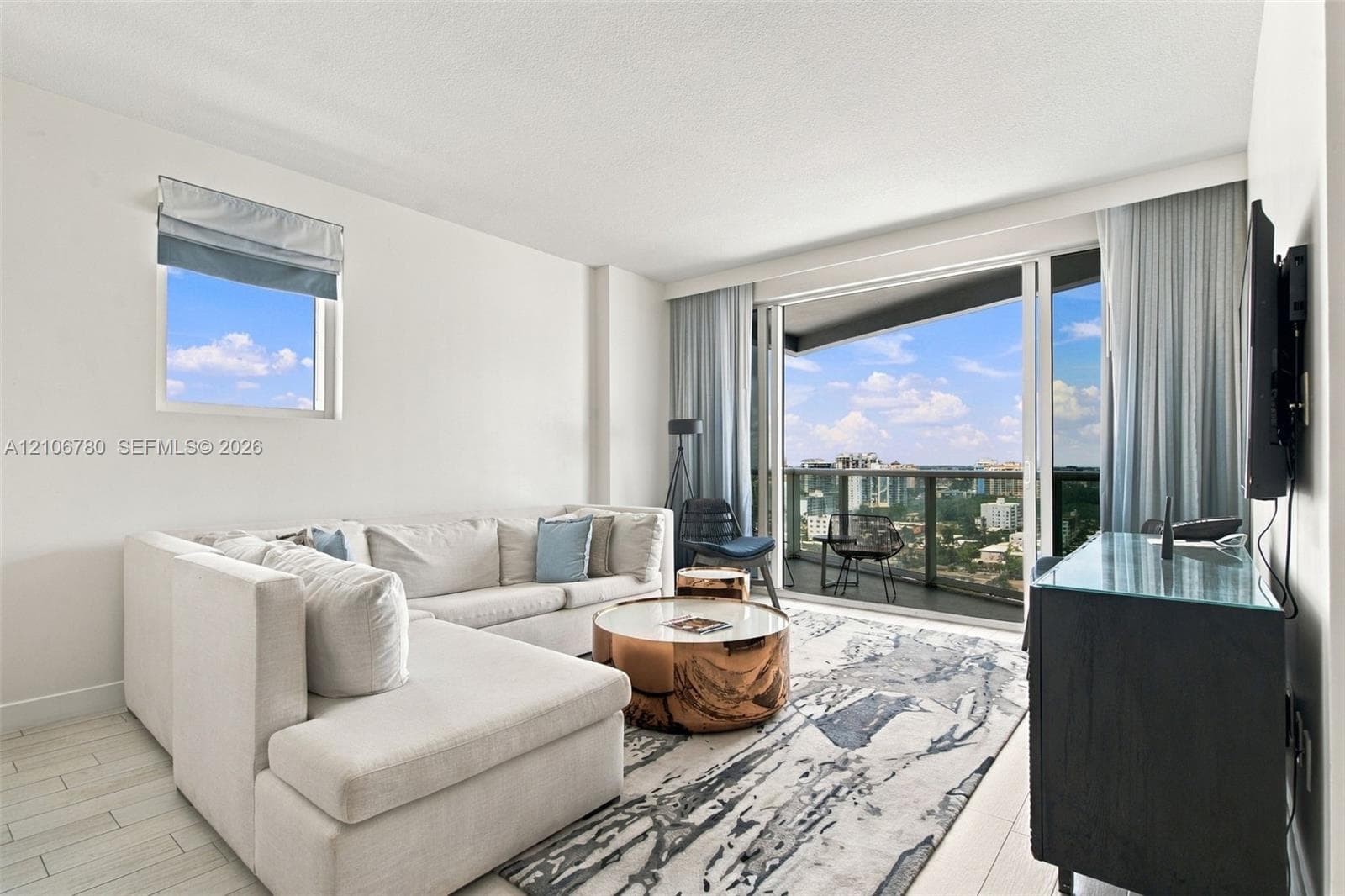 Floor-to-ceiling sliding glass door, private balcony with metal railing, light-tone wood-finish flooring, and expansive wall of windows