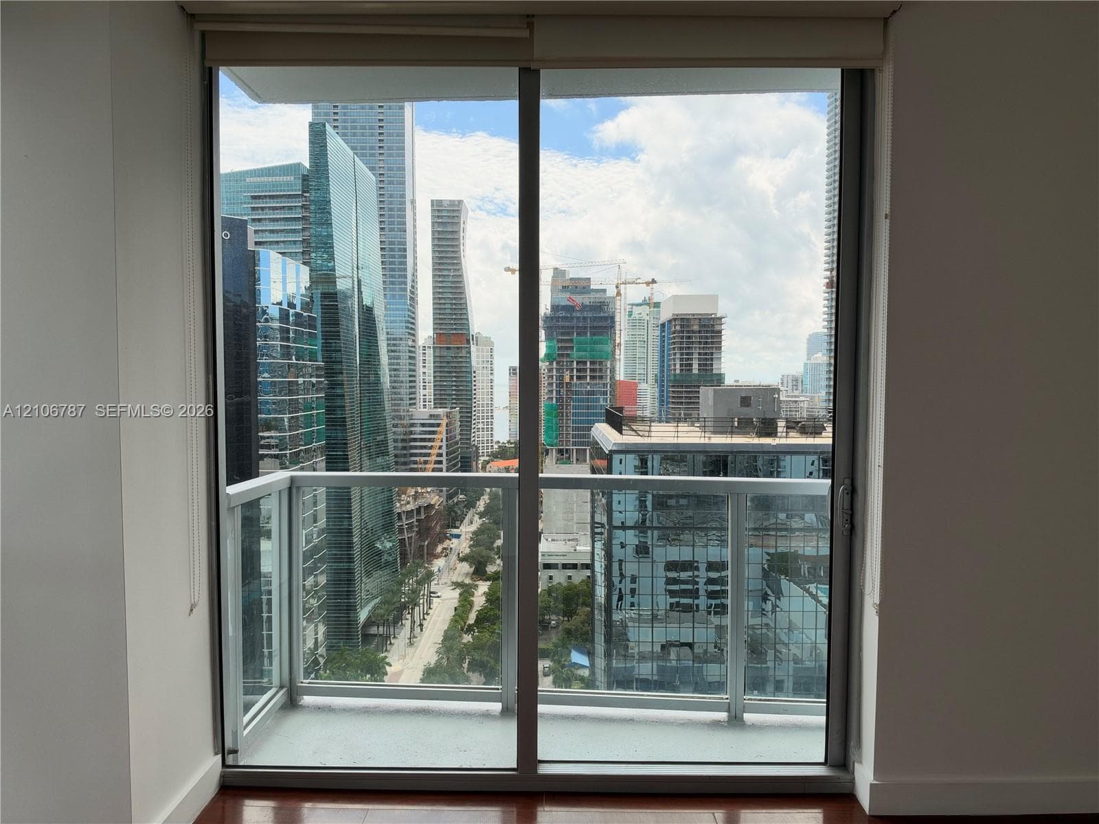 Floor-to-ceiling sliding glass door, private balcony with metal and glass railing, and panoramic city skyline backdrop
