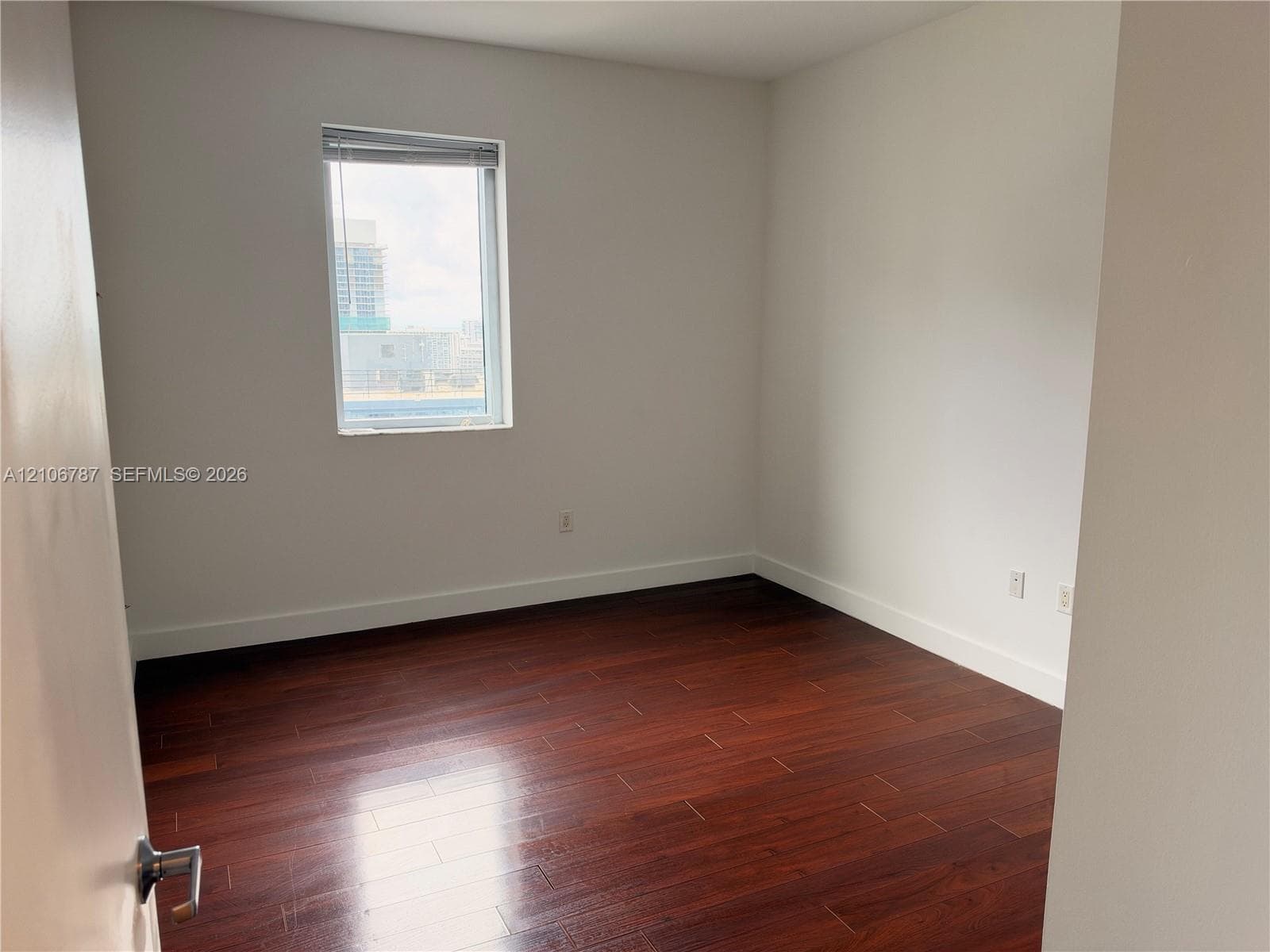 Room featuring wood-finish flooring, white walls, and a single-pane window with blinds