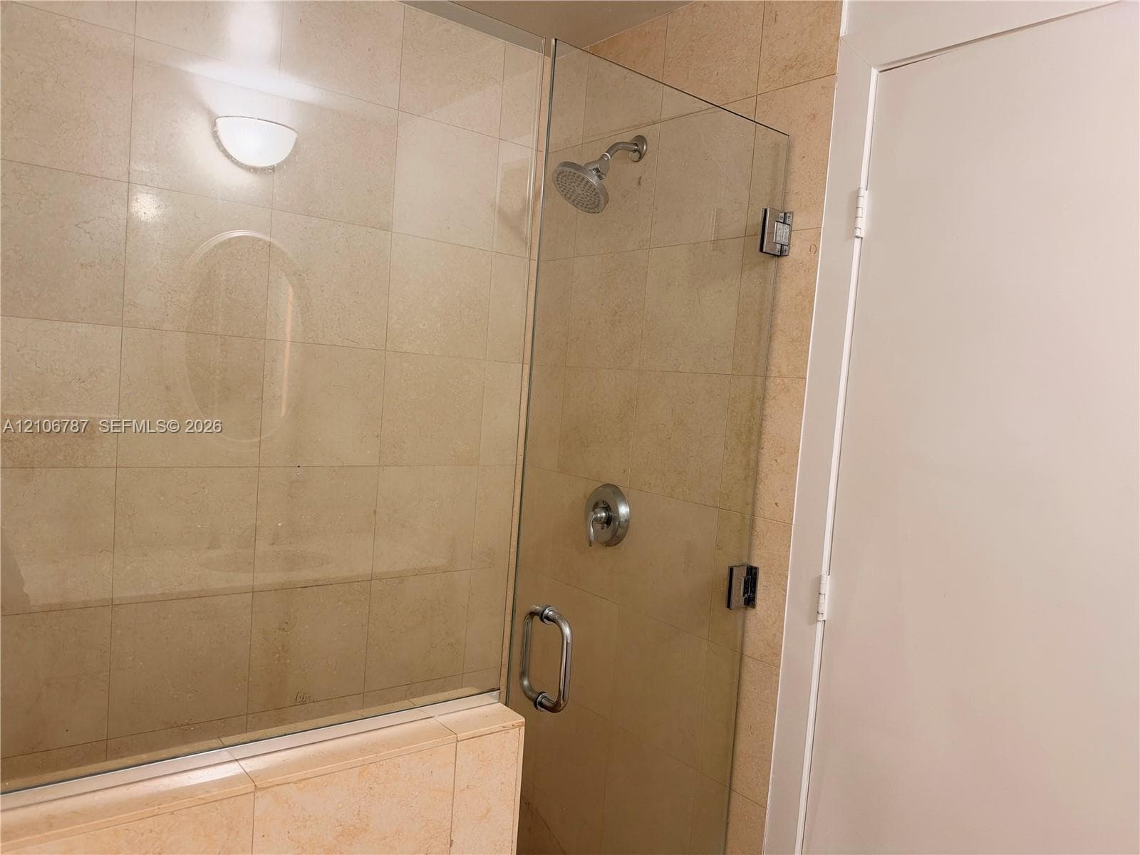 Walk-in shower enclosure featuring light-toned stone tile surround, frameless glass door, wall-mounted showerhead, and polished chrome fixtures