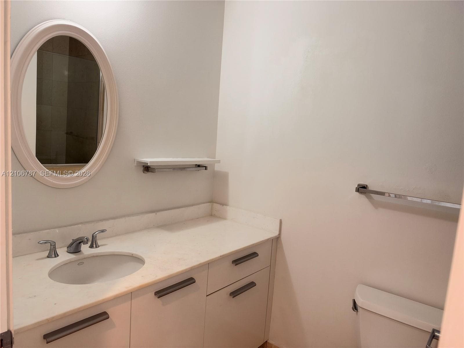 Bathroom vanity featuring a light-toned countertop with an integrated basin, chrome widespread faucet, white cabinetry with horizontal hardware, and an oval wall-mounted mirror