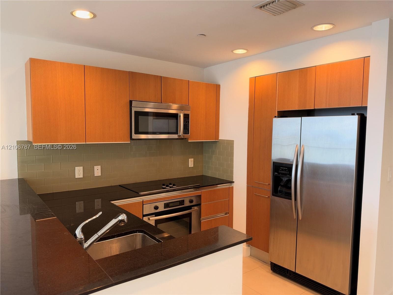 Kitchen featuring wood-finish flat-panel cabinetry, dark solid-surface countertops, subway tile backsplash, stainless steel appliances, and recessed lighting