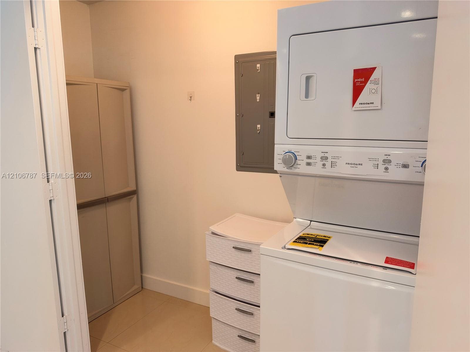 Utility space featuring a stacked washer and dryer unit, neutral tile flooring, and a recessed electrical service panel