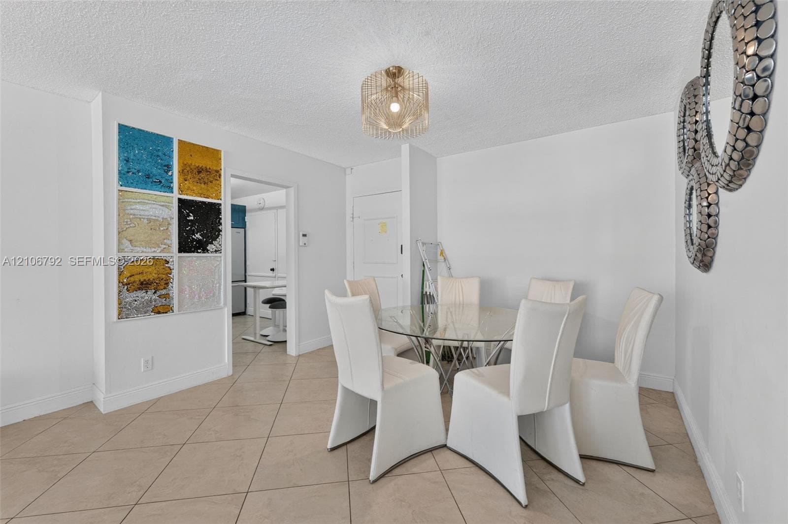 Interior space featuring neutral tile flooring, a tiered metal chandelier, and a decorative wall accent composed of multi-colored textured panels