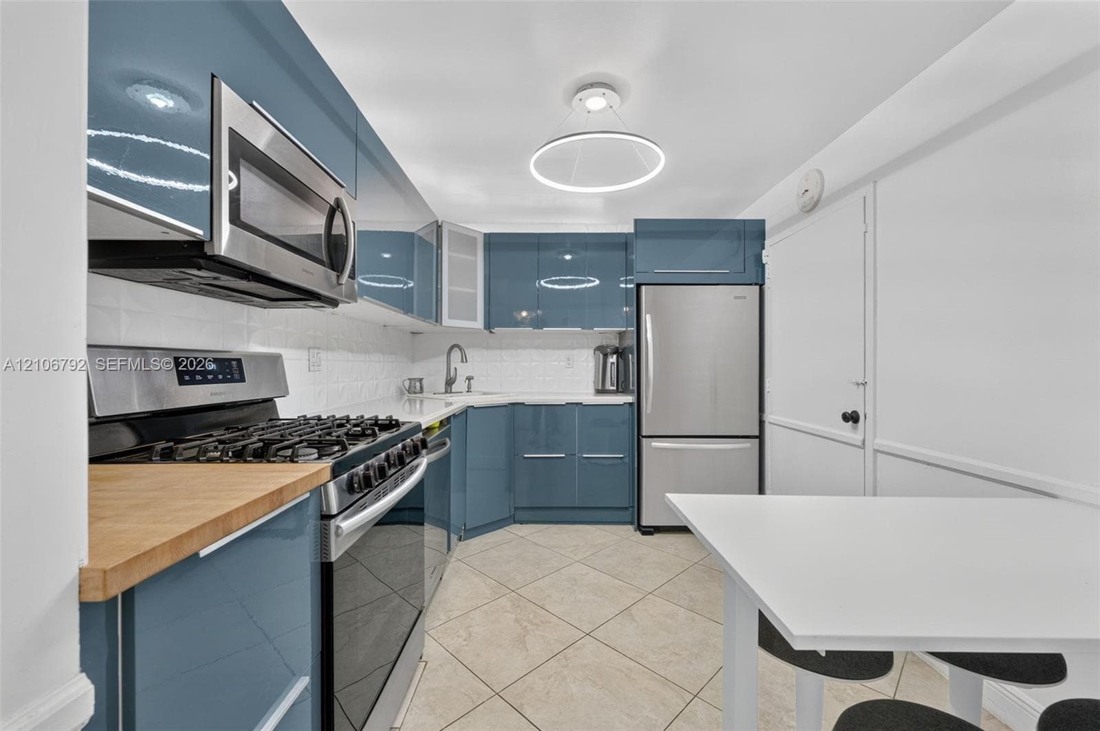 Glossy blue cabinetry featuring flat-panel doors, stainless steel appliances, butcher block countertops, white tiled backsplash, and circular LED overhead lighting