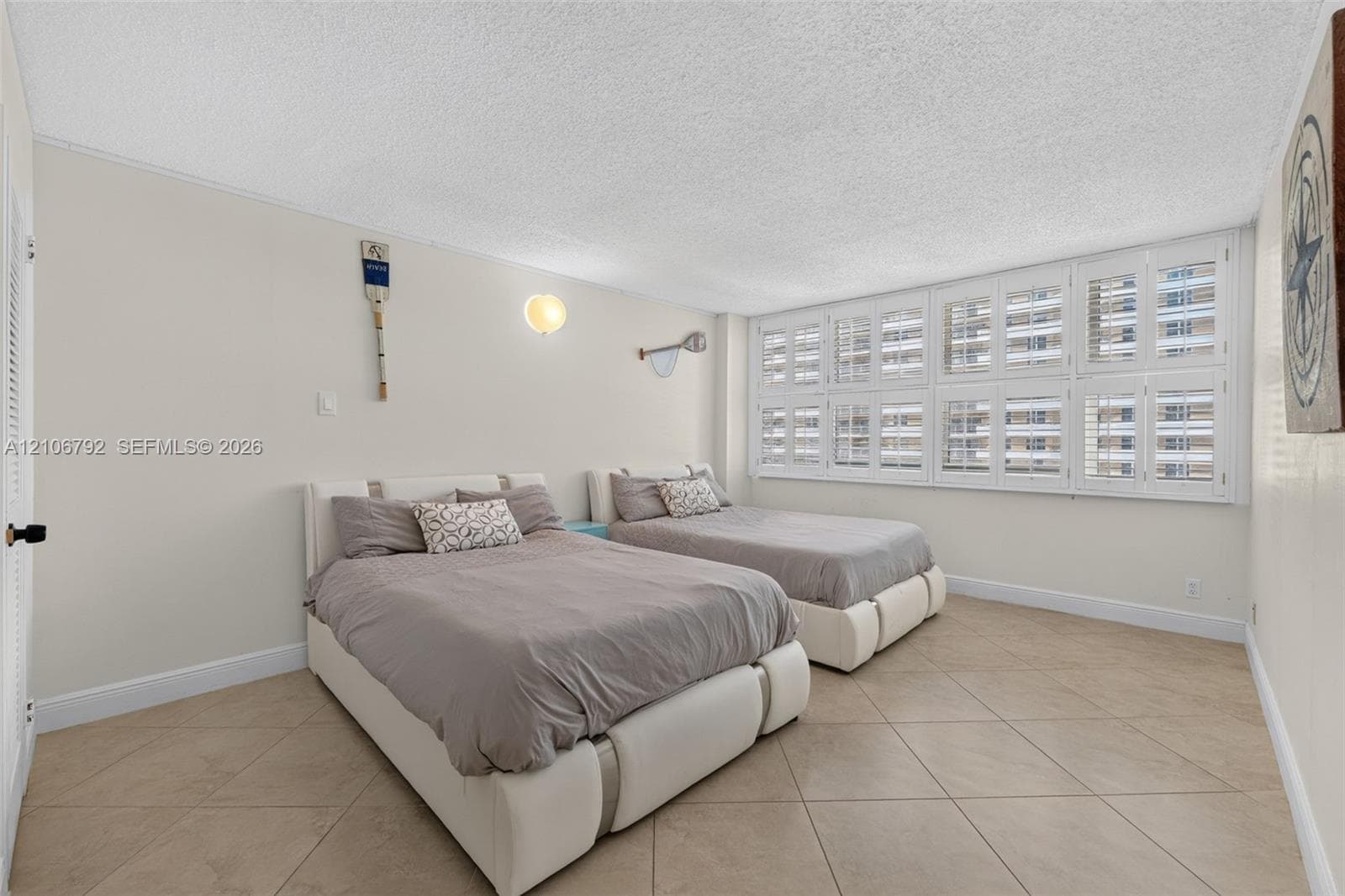 Neutral interior space featuring large-format diagonal tile flooring, white plantation shutters, and a wall-mounted light fixture