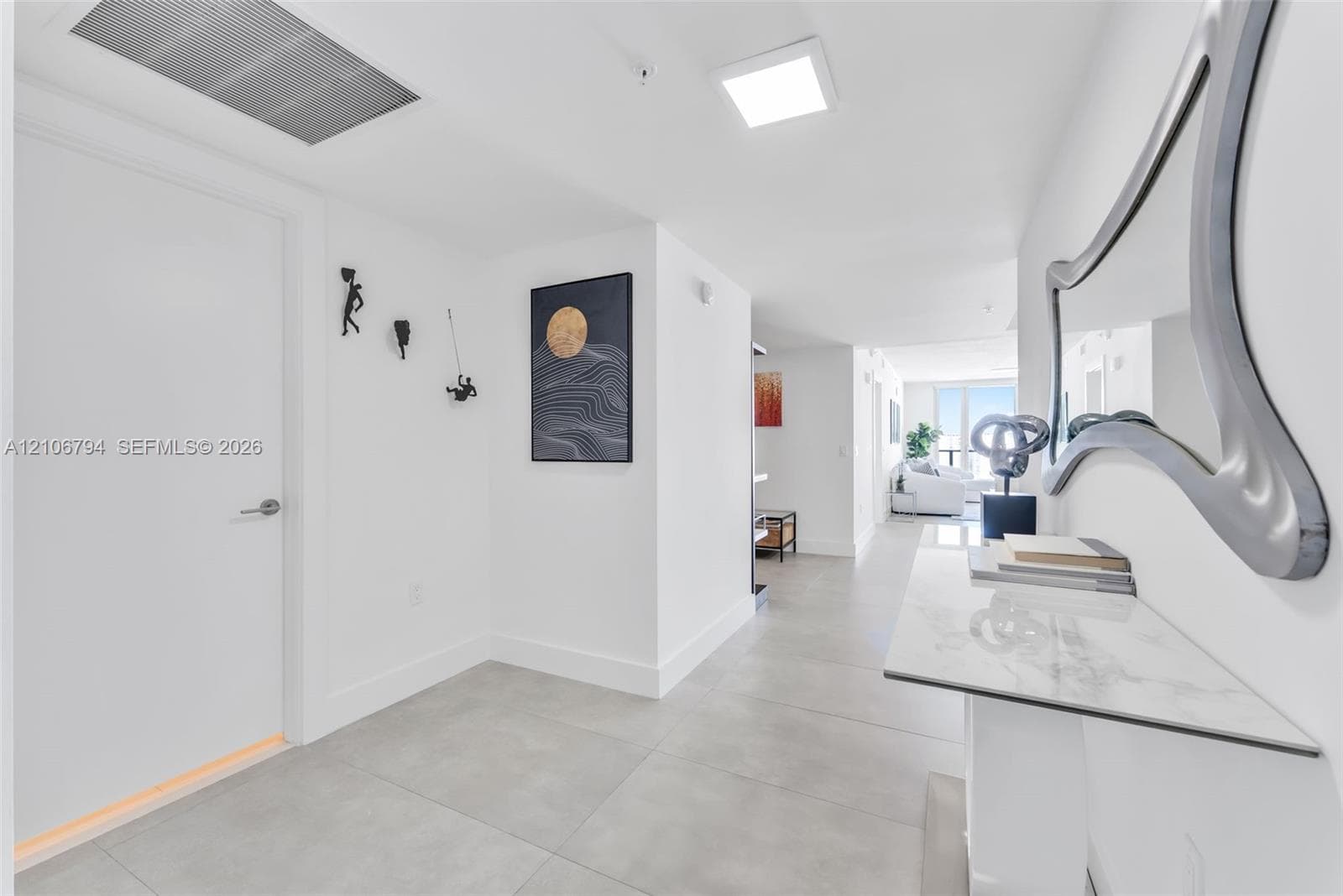 Interior hallway featuring large-format ceramic tile flooring, recessed square ceiling lighting, and crisp white wall finishes