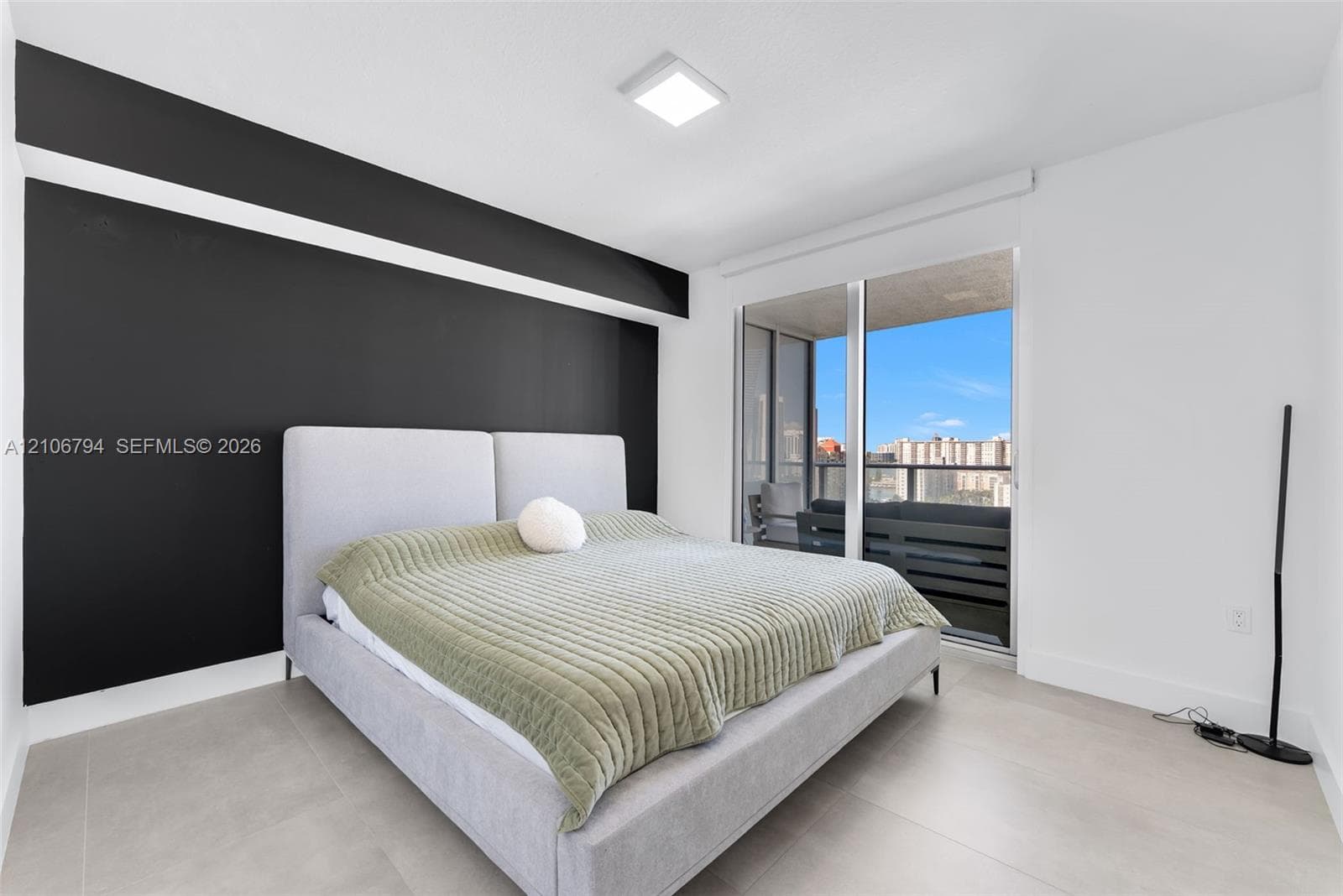 Interior space featuring large-format tile flooring, a prominent black accent wall, and floor-to-ceiling glass sliding doors opening to a balcony