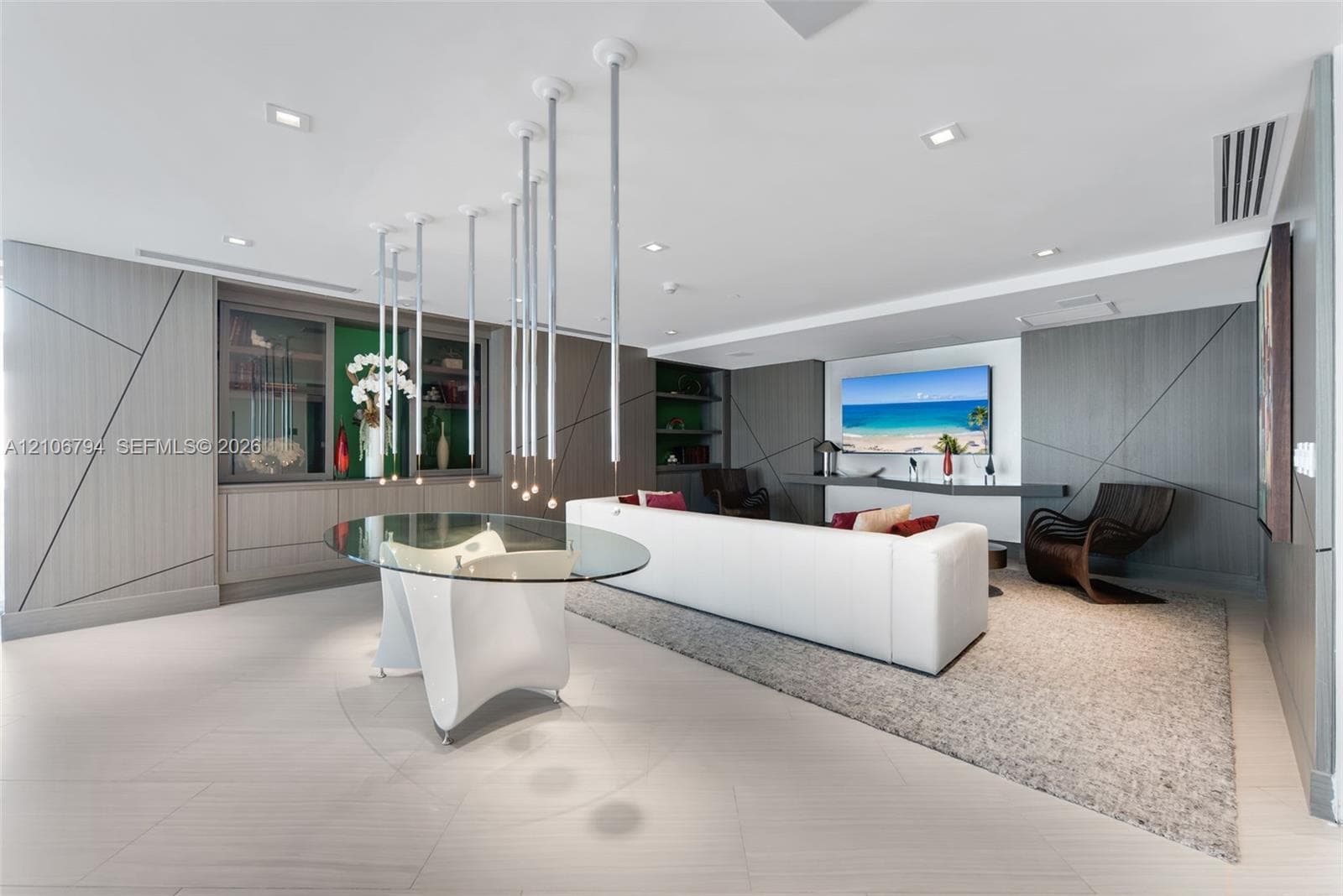 Open-concept area featuring large-format tile flooring, custom wall paneling with geometric detailing, built-in cabinetry, and a tiered pendant lighting fixture