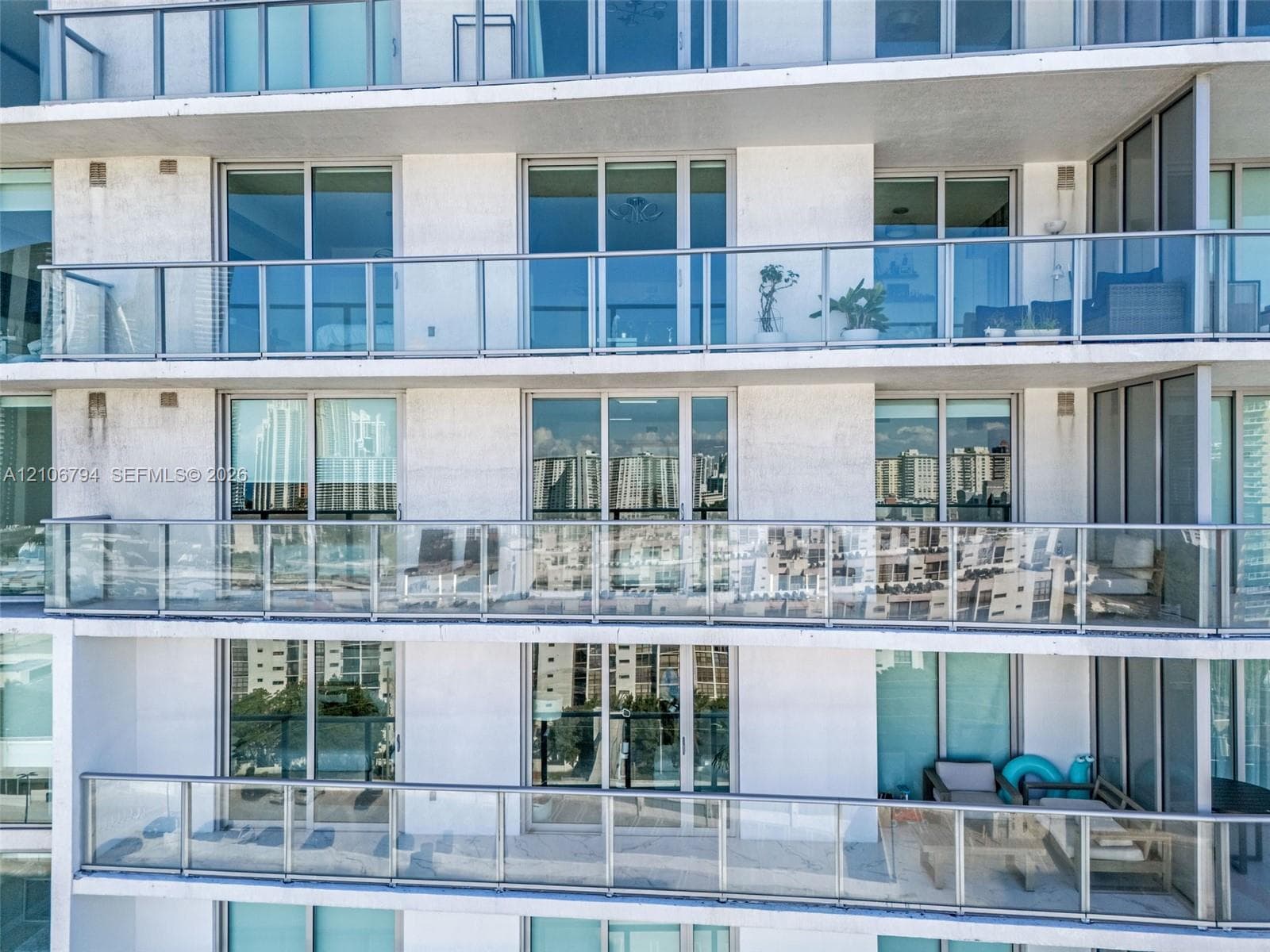 High-rise building exterior featuring private glass-railed balconies and floor-to-ceiling sliding glass doors