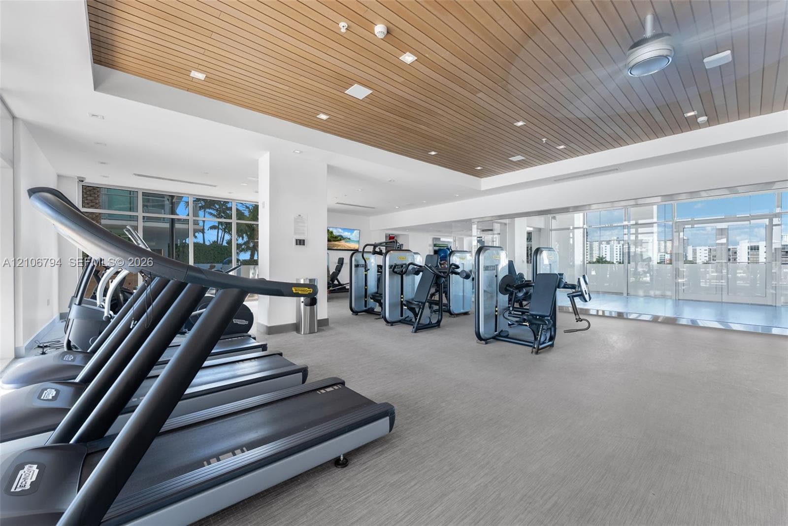 Fitness center featuring wood-slat ceiling, recessed lighting, floor-to-ceiling glass windows, and textured flooring