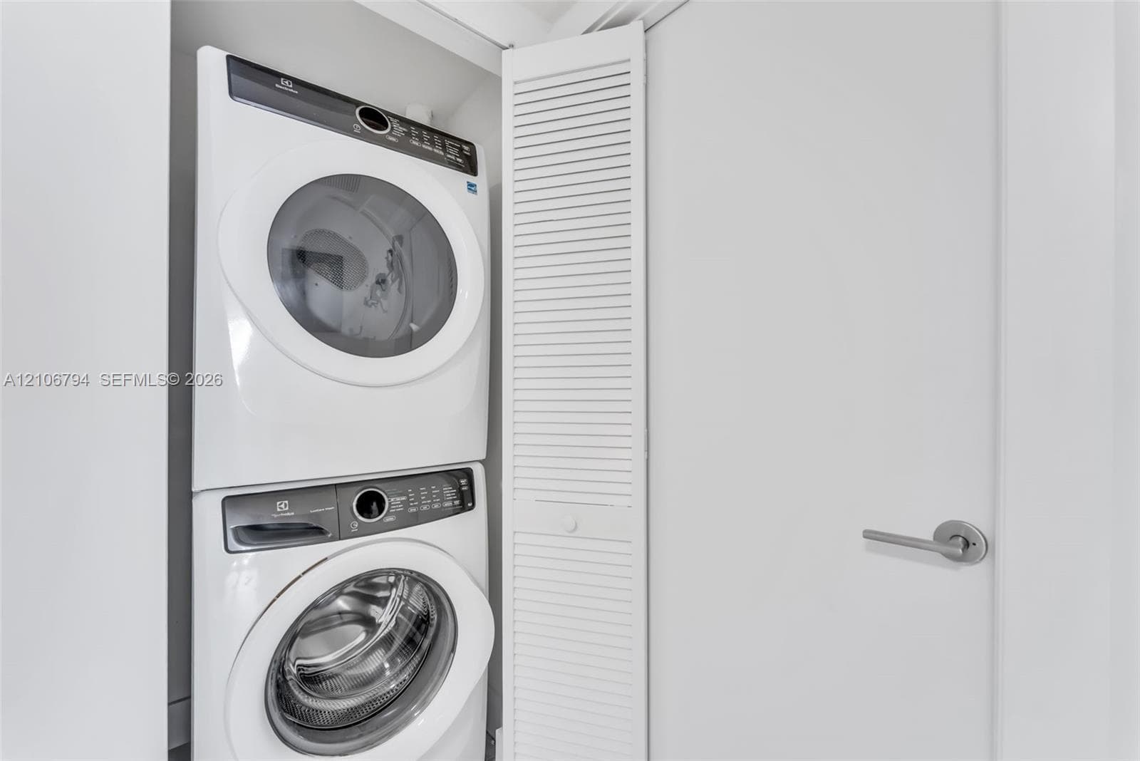 Stacked front-load laundry appliances enclosed by white louvered doors