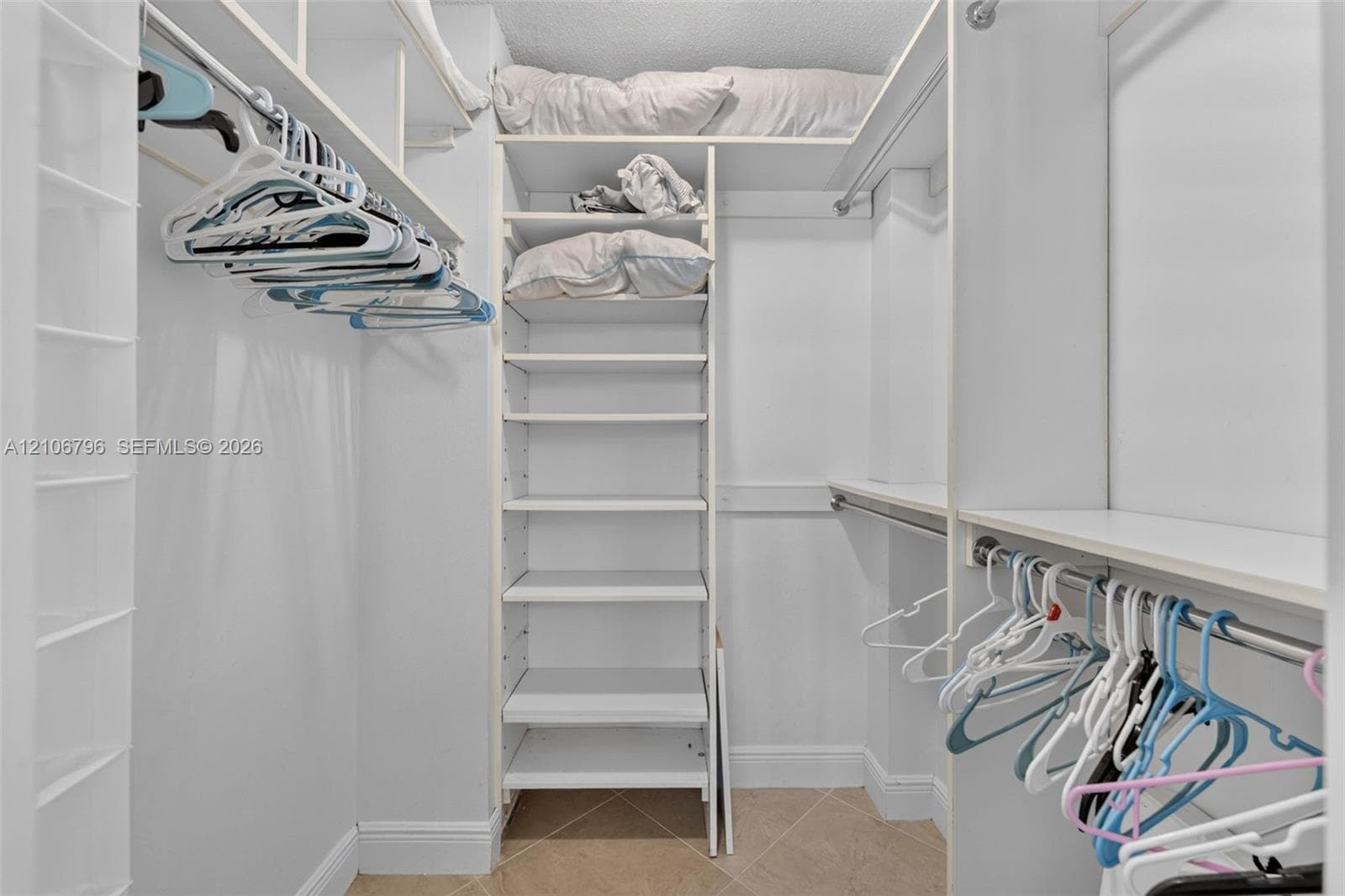 Walk-in closet featuring white built-in shelving, multiple hanging rods, and tile flooring