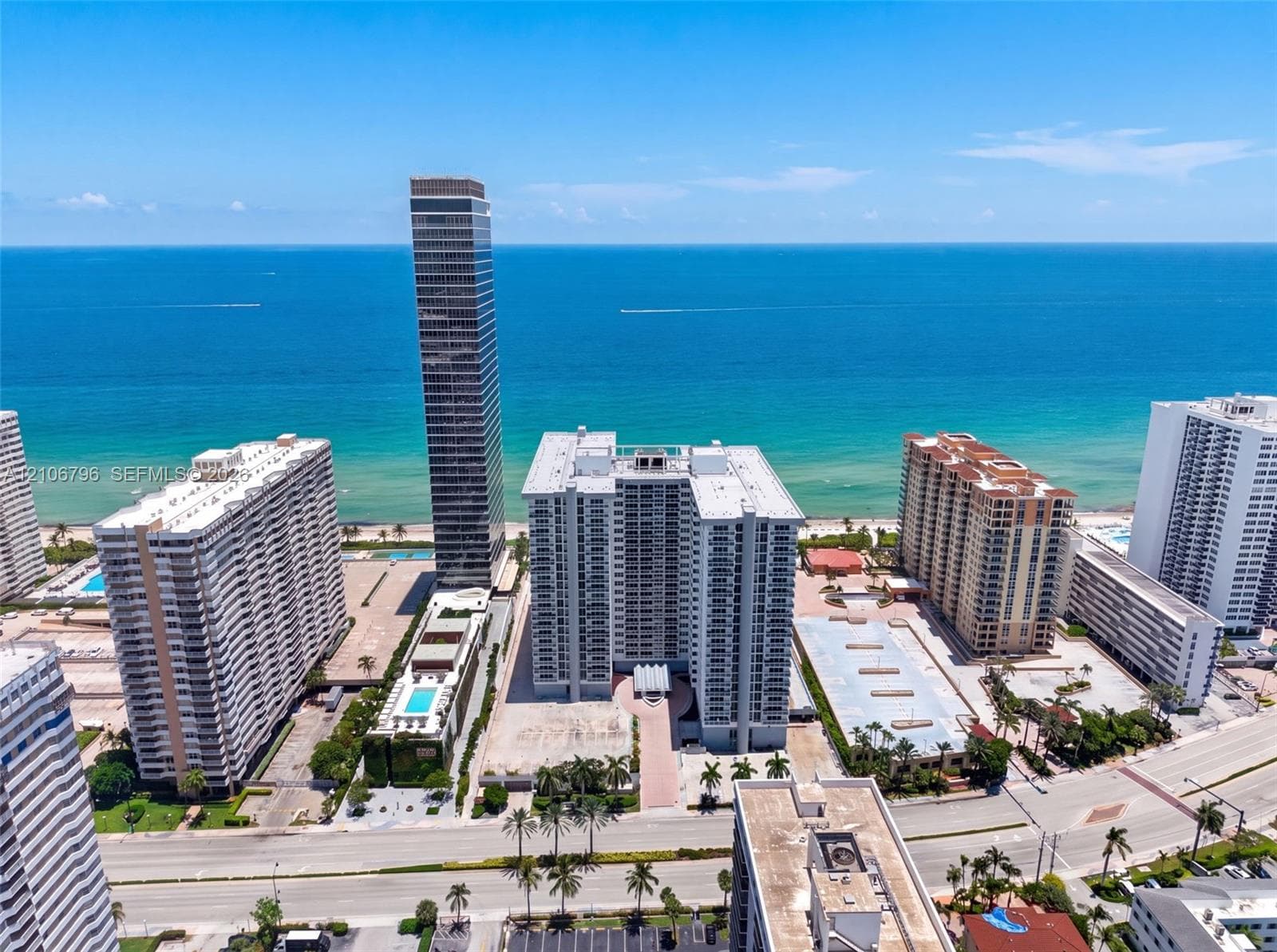 Aerial perspective of oceanfront high-rise residential properties featuring immediate proximity to the coastline, landscaped grounds, and paved parking areas