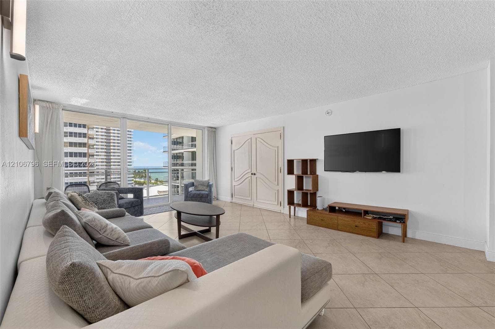 Large-format tile flooring, double interior doors with molded panel detailing, and floor-to-ceiling glass sliding doors opening to an exterior balcony