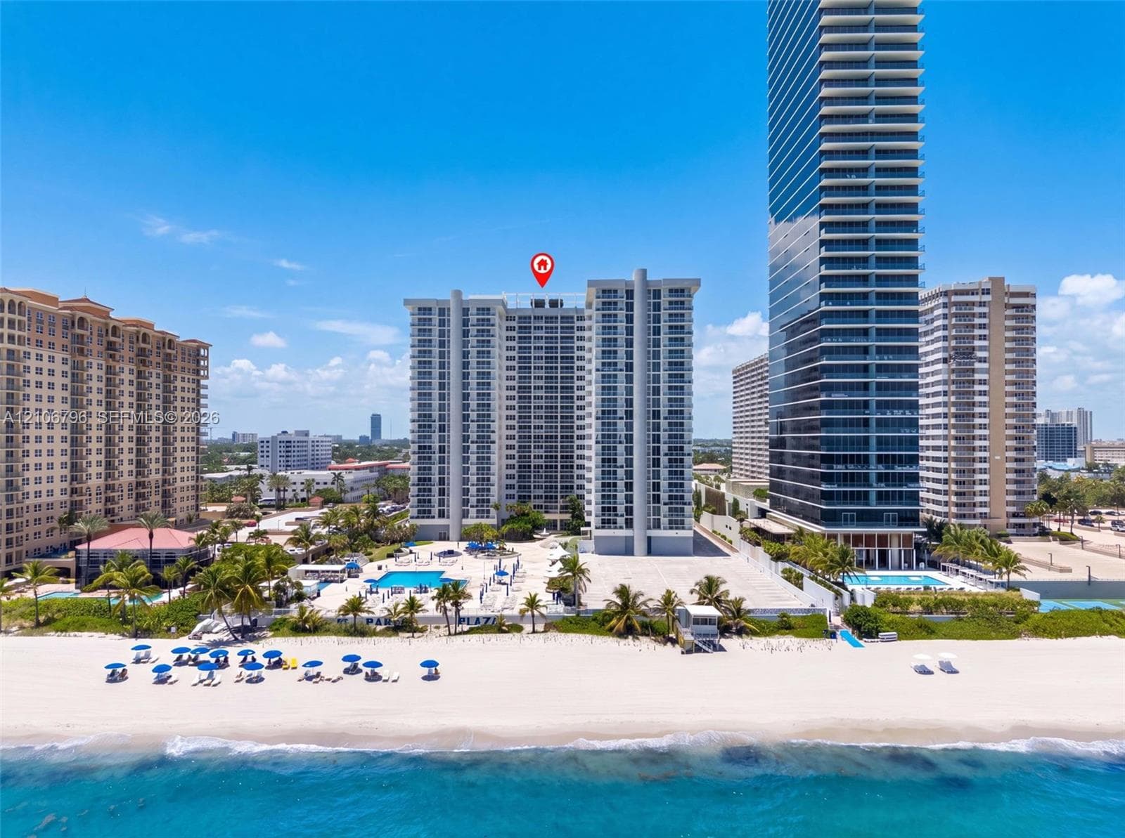 High-rise condominium building featuring direct beach access, an outdoor swimming pool, a sun deck, and mature palm landscaping