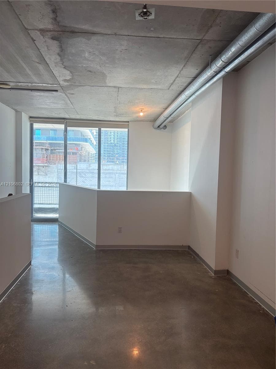 Industrial-style interior featuring exposed concrete ceilings, polished concrete flooring, floor-to-ceiling windows, and exposed metallic ductwork